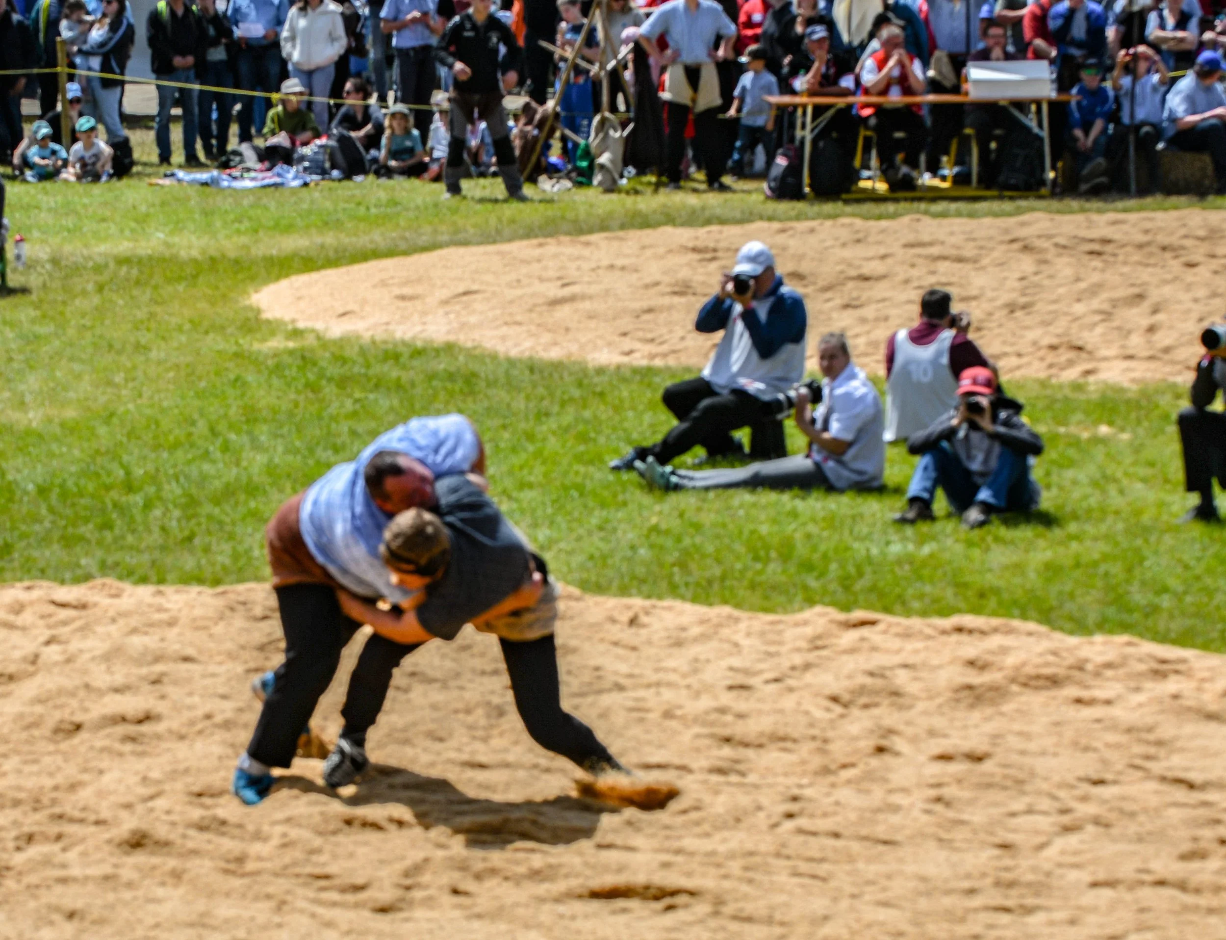 Menschen beim Sandkastenspiel bei einem Festival, mit Zuschauern im Hintergrund, einige Fotografen, und ein Kind, das im Sand spielt.