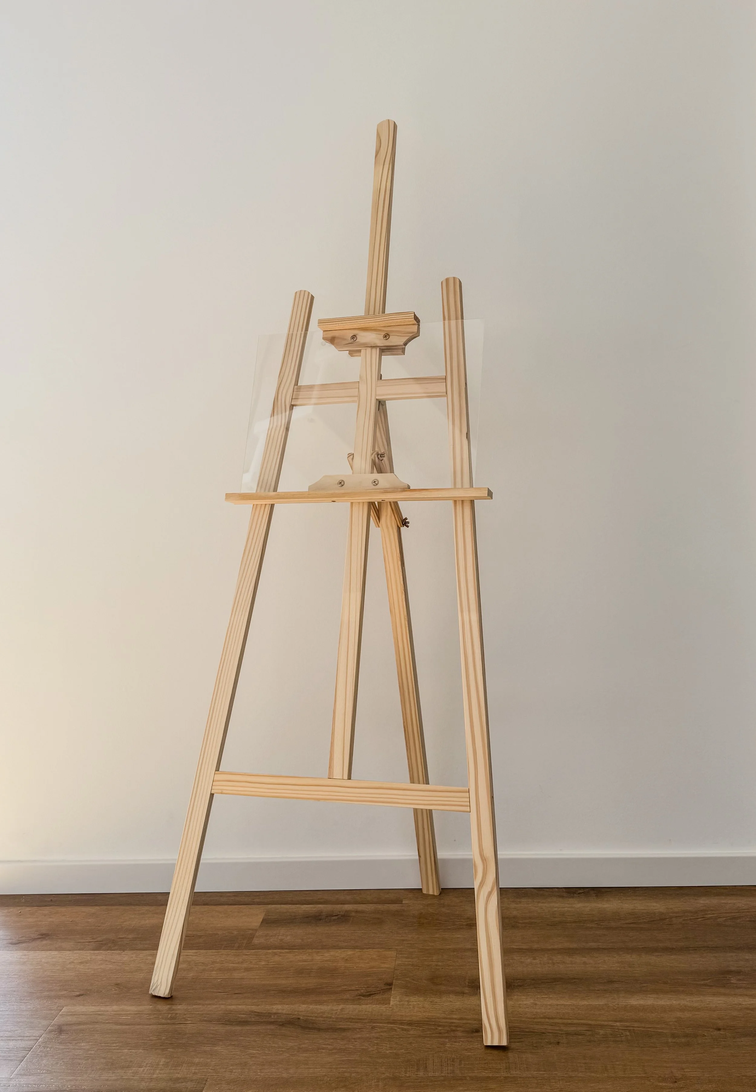Ein unbemalter Holzstaffelei steht vor einer weißen Wand auf einem Holzboden.