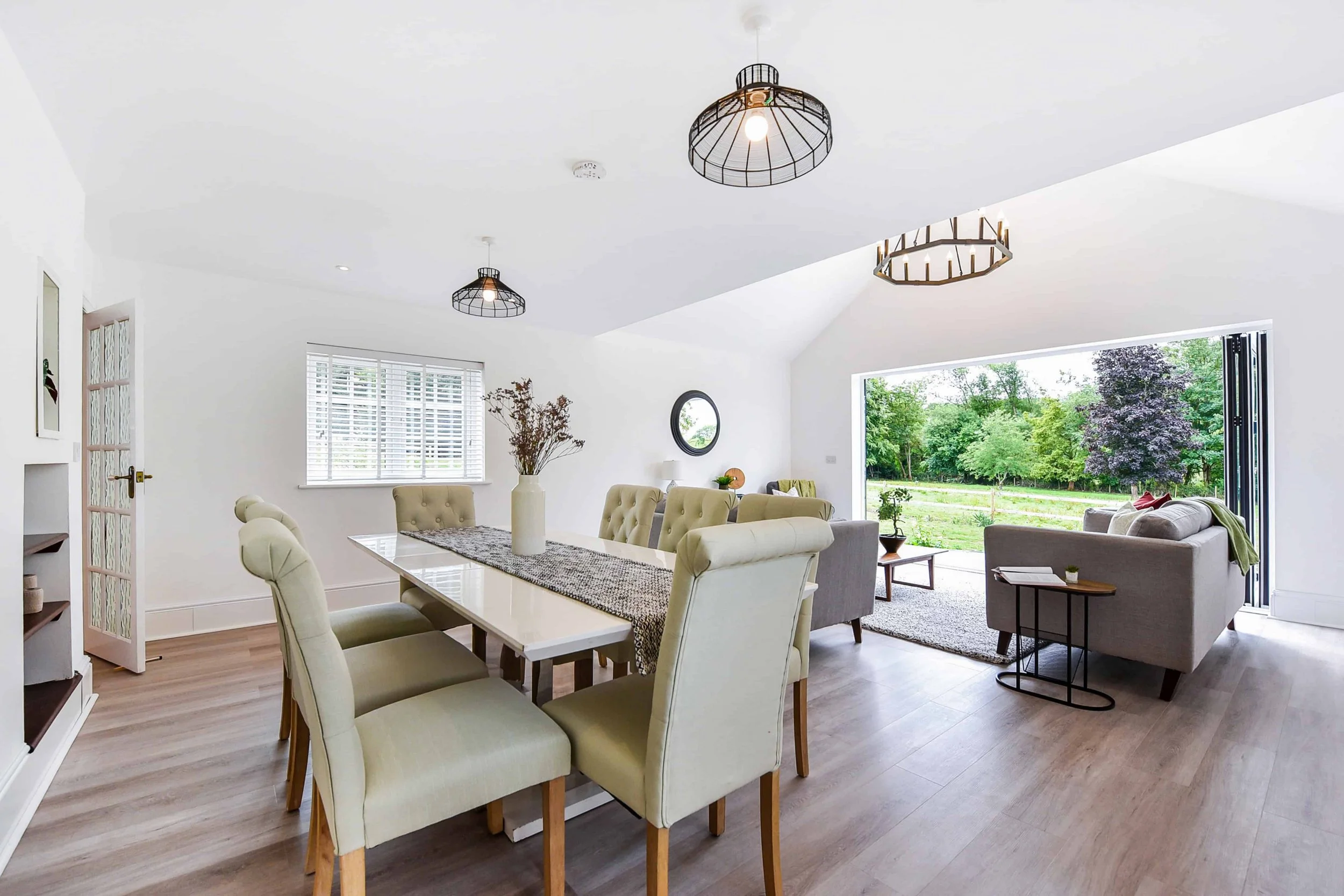 A bright, open plan modern living and dining room with vaulted ceiling and bi-fold doors to the patio. Reclaimed wooden floor boards, decorative skirting boards and feature light fittings