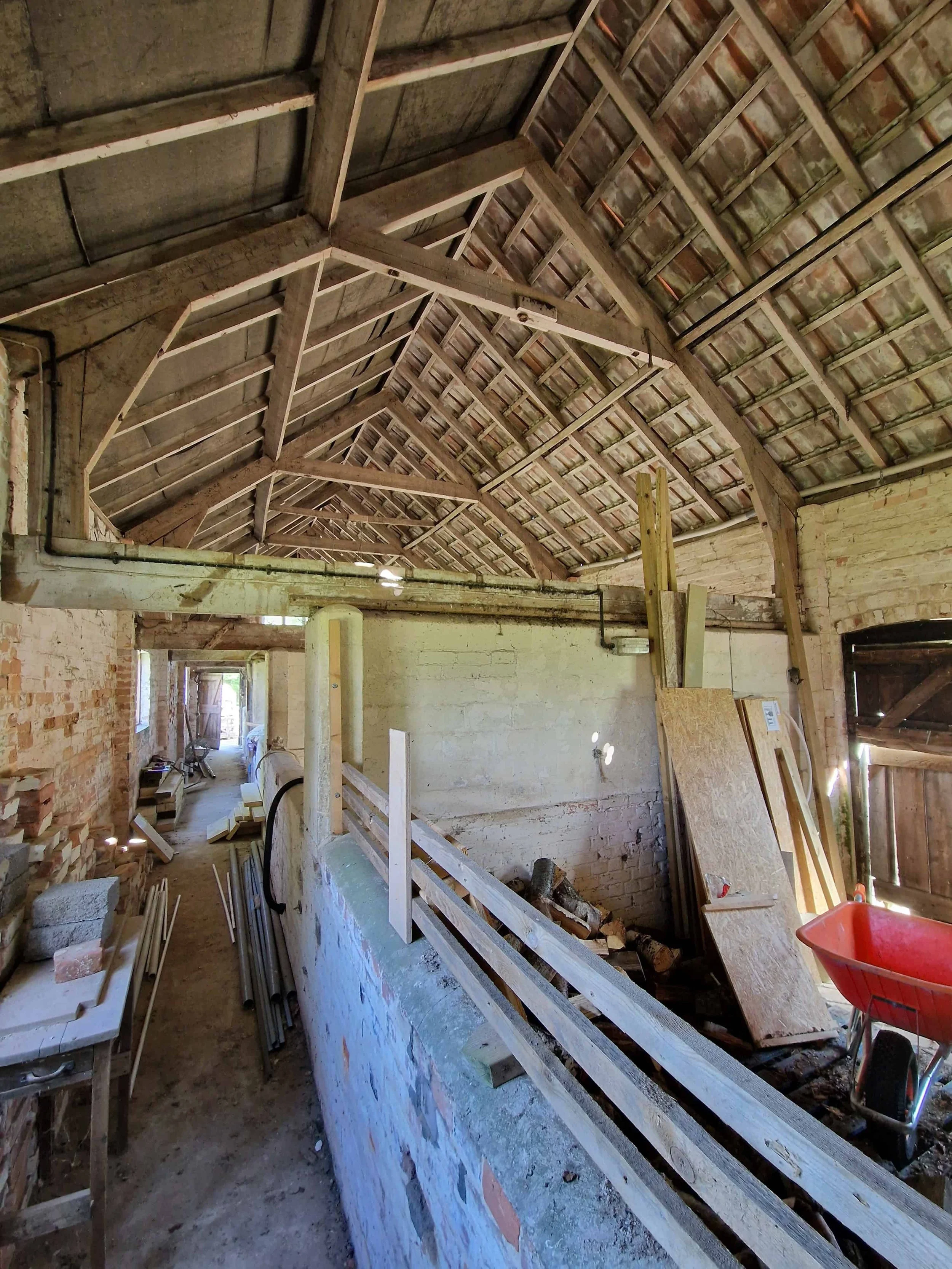 Interior of a listed historic barn conversion building with visible wooden roof trusses, exposed timber rafters, vaulted ceilings, brick walls, timber doors and windows.