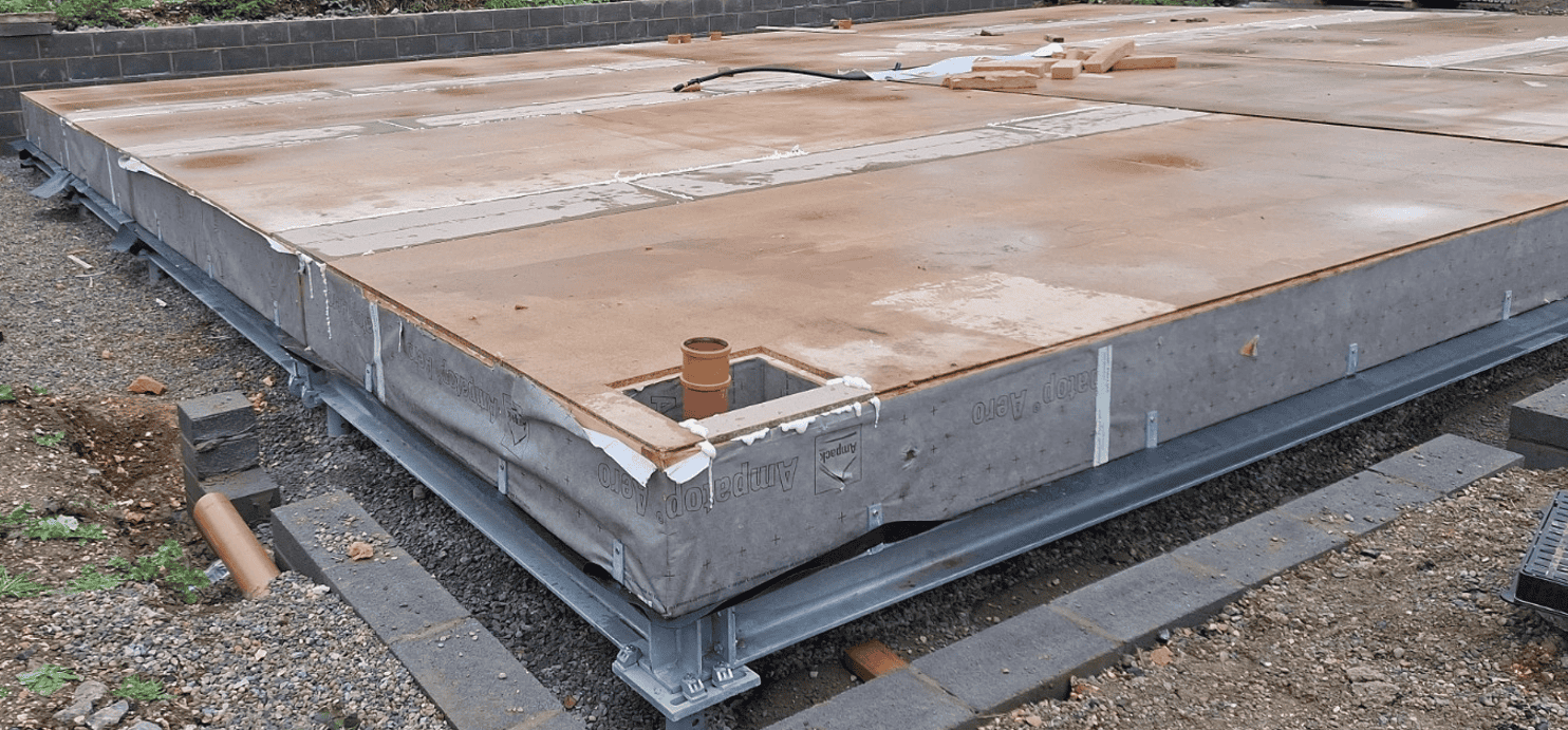 Construction site with a raised foundation, SIPS panel wooden suspended floor, and metal sub-framing, surrounded by gravel and paving stones.