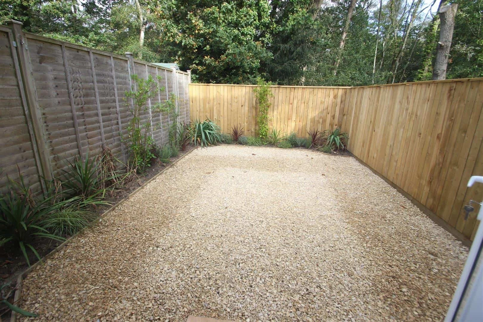 A gravel garden in a rented property upgraded with new wooden fence, garden plants along the edges, and trees in the background.