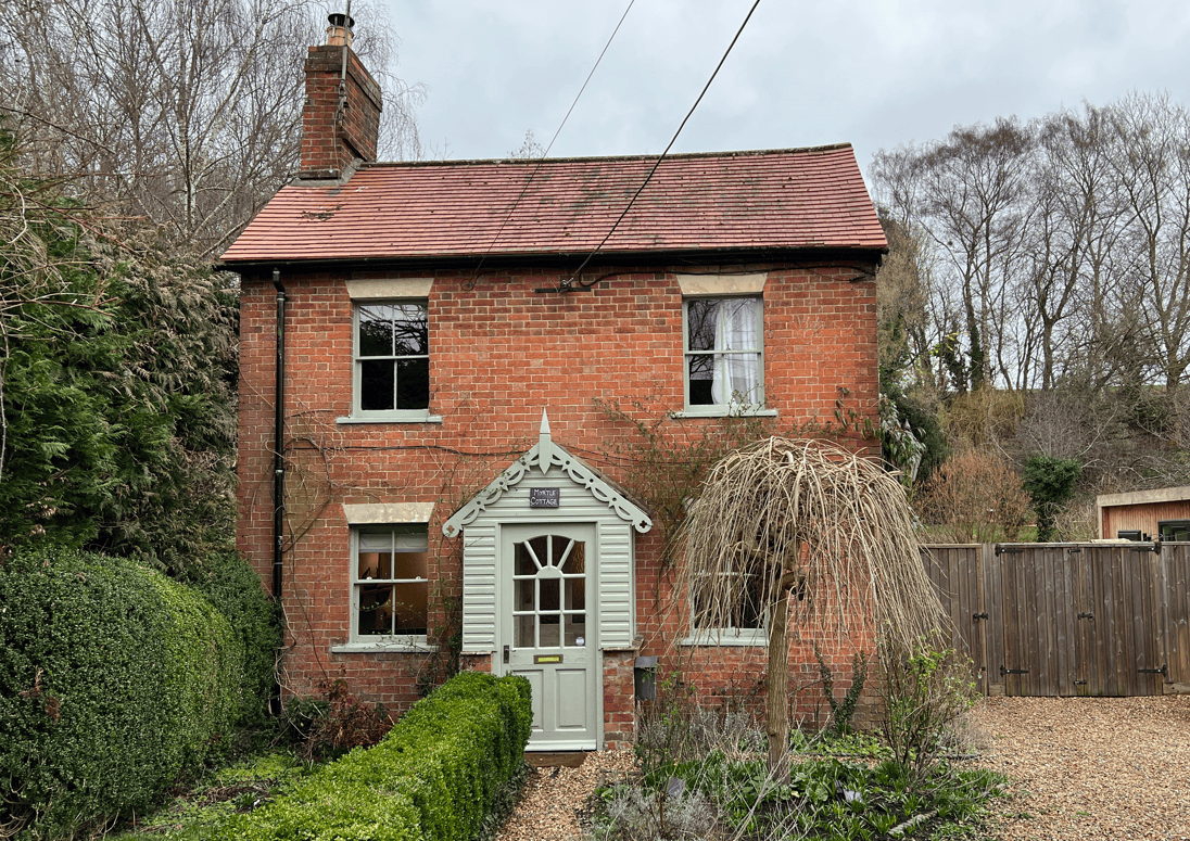 Two-storey traditional Victorian brick cottage with a clay tiled roof, recessed casement windows with stone arched lintels, decorative white timber front door and porch, one chimney, historic details.