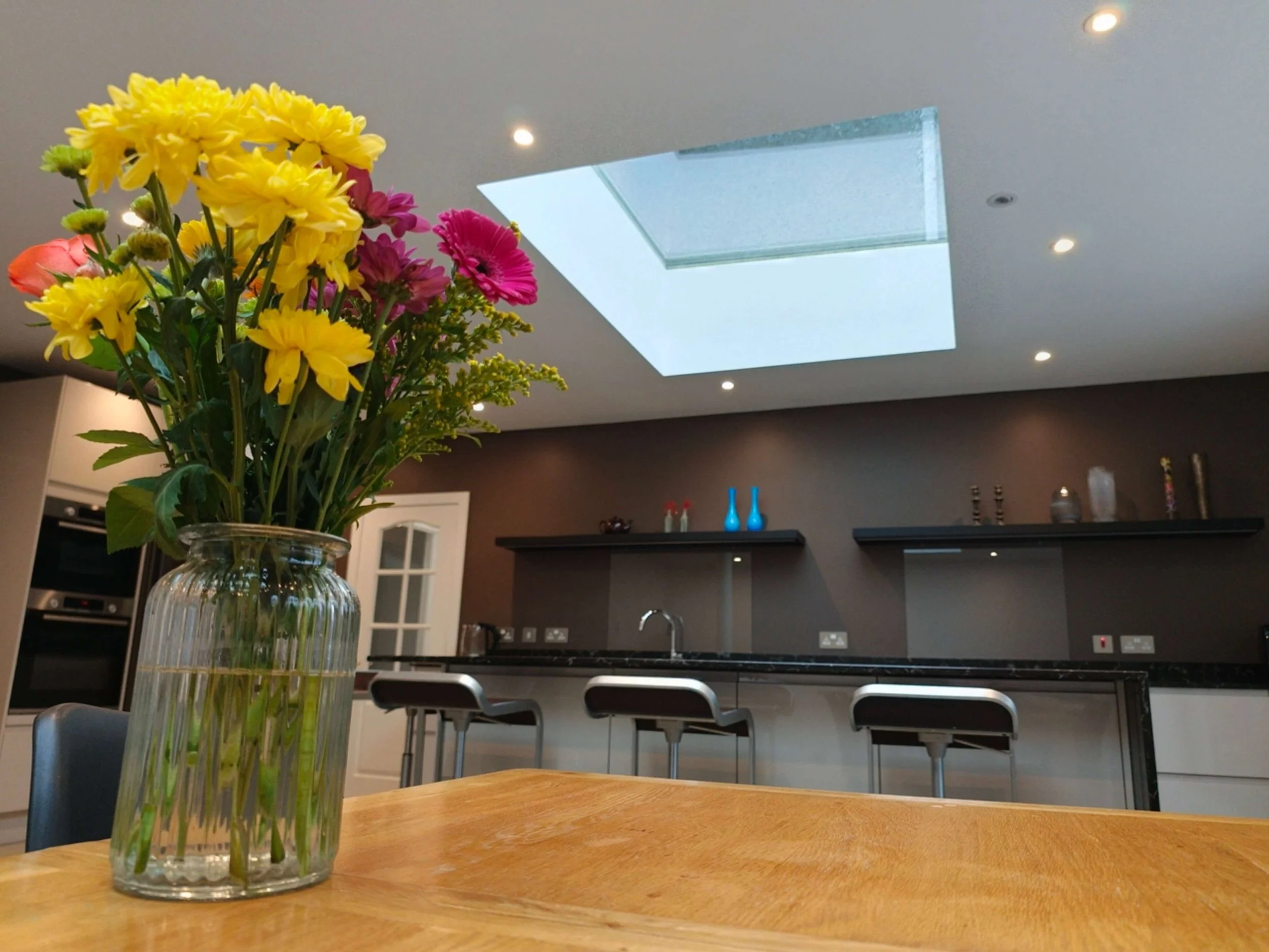 Open plan kitchen and dining room extension, modern kitchen island with bar stools, corian worktops, recessed ceiling spotlights, frameless glazed rooflights.