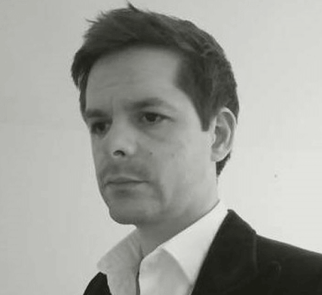 Black and white photo of a man from imj architecture with short dark hair wearing a white shirt and a dark blazer, facing slightly to the right.