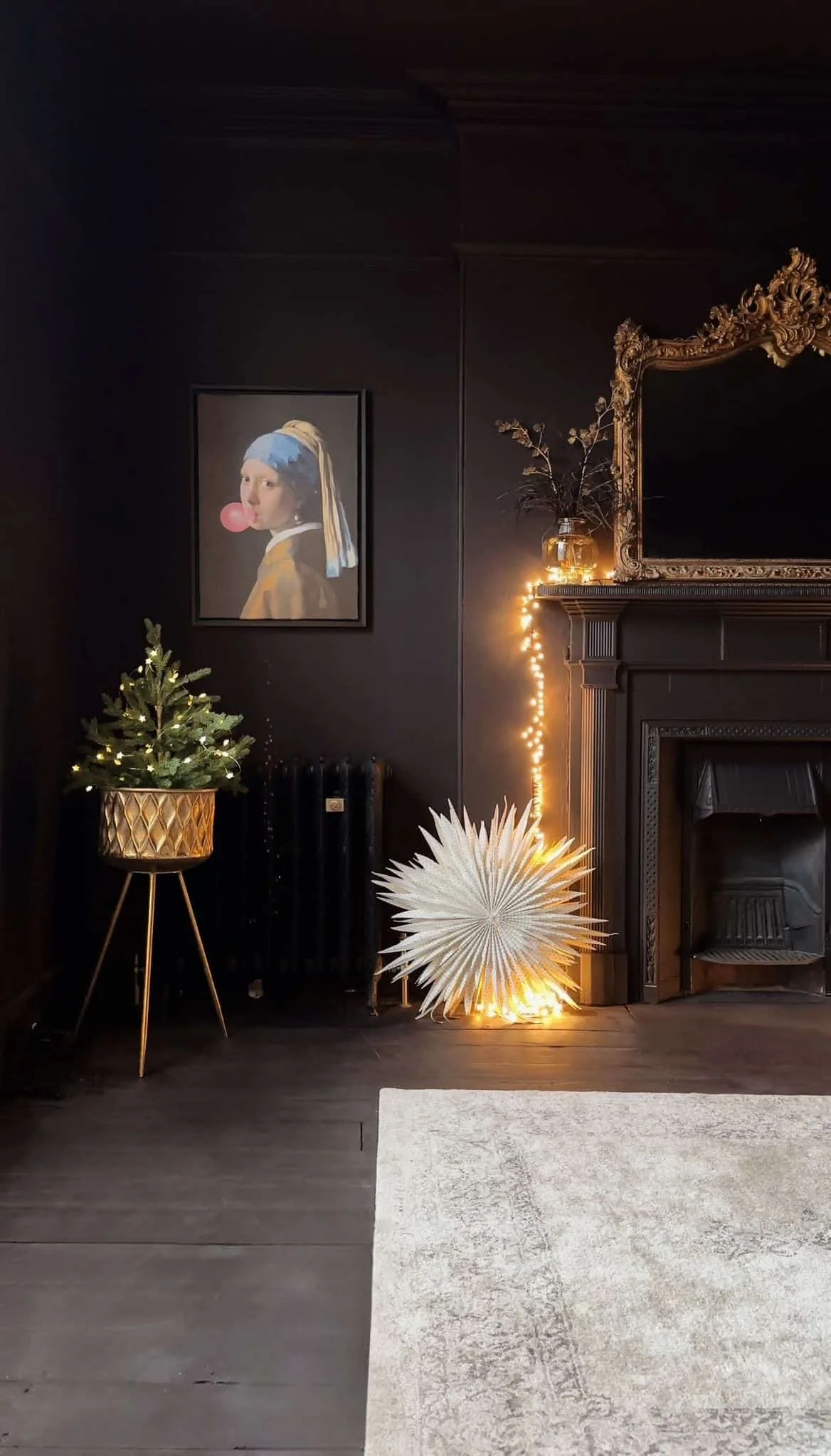 Cozy living room snug corner, dark painted interior design, a large ornate gold mirror above a traditional cast iron fireplace with historic detailed timber surround.