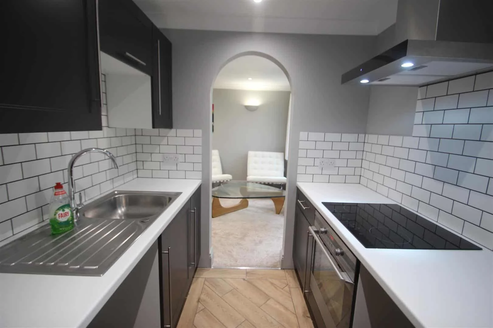 New modern kitchen renovation in a rented property with dark cabinets, white countertops, white subway tile backsplash, sink with faucet, stovetop, range hood, energy efficient LED lighting, new insulation, new double glazed windows and doors.