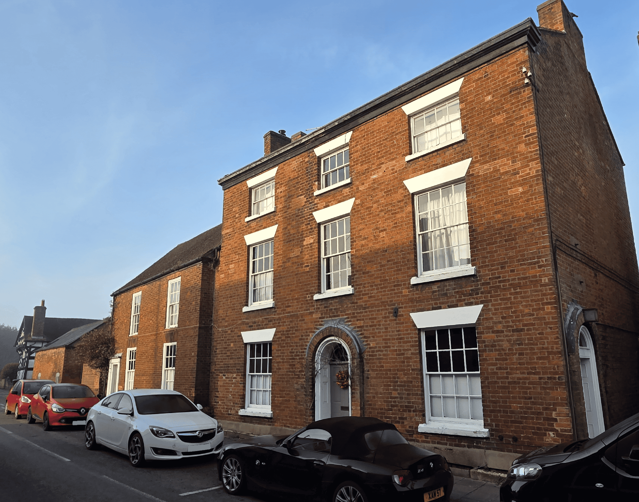 A listed Georgian townhouse with brick walls, traditional timber sash windows, slate roof, a painted timber front door, eaves cornice, two chimney stacks, traditional painted metal guttering, stone window cills, set on the street.