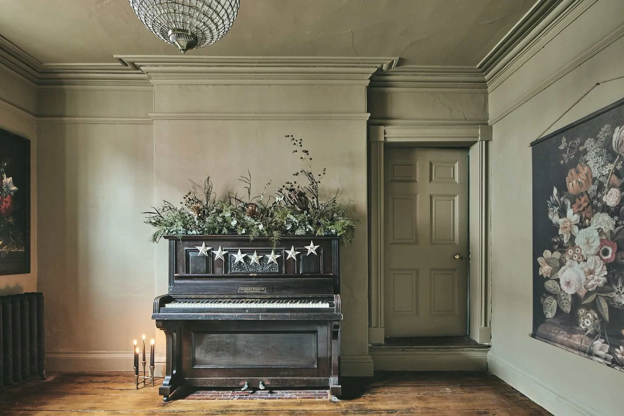 Music room with vintage black piano, refurbished sanded floorboards, original historic skirting boards and picture rails, plaster ceiling rose, sash window shutters and wall panelling, chandelier light fitting.