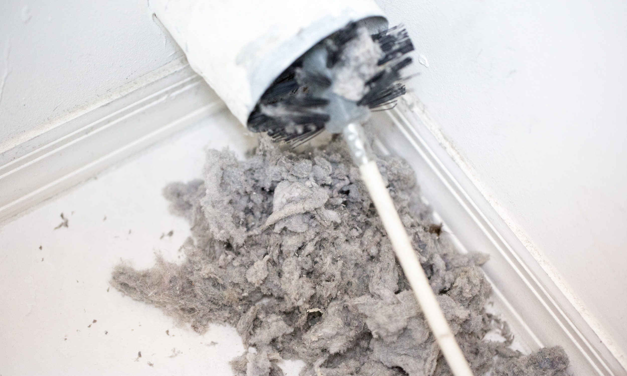 Debris and dust from a ceiling vent or duct falling onto the floor with a dust brush nearby.