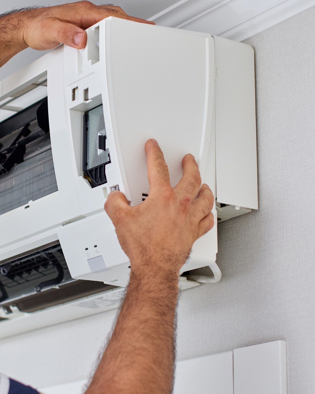 Person removing the front cover of an air conditioning unit mounted on a wall.