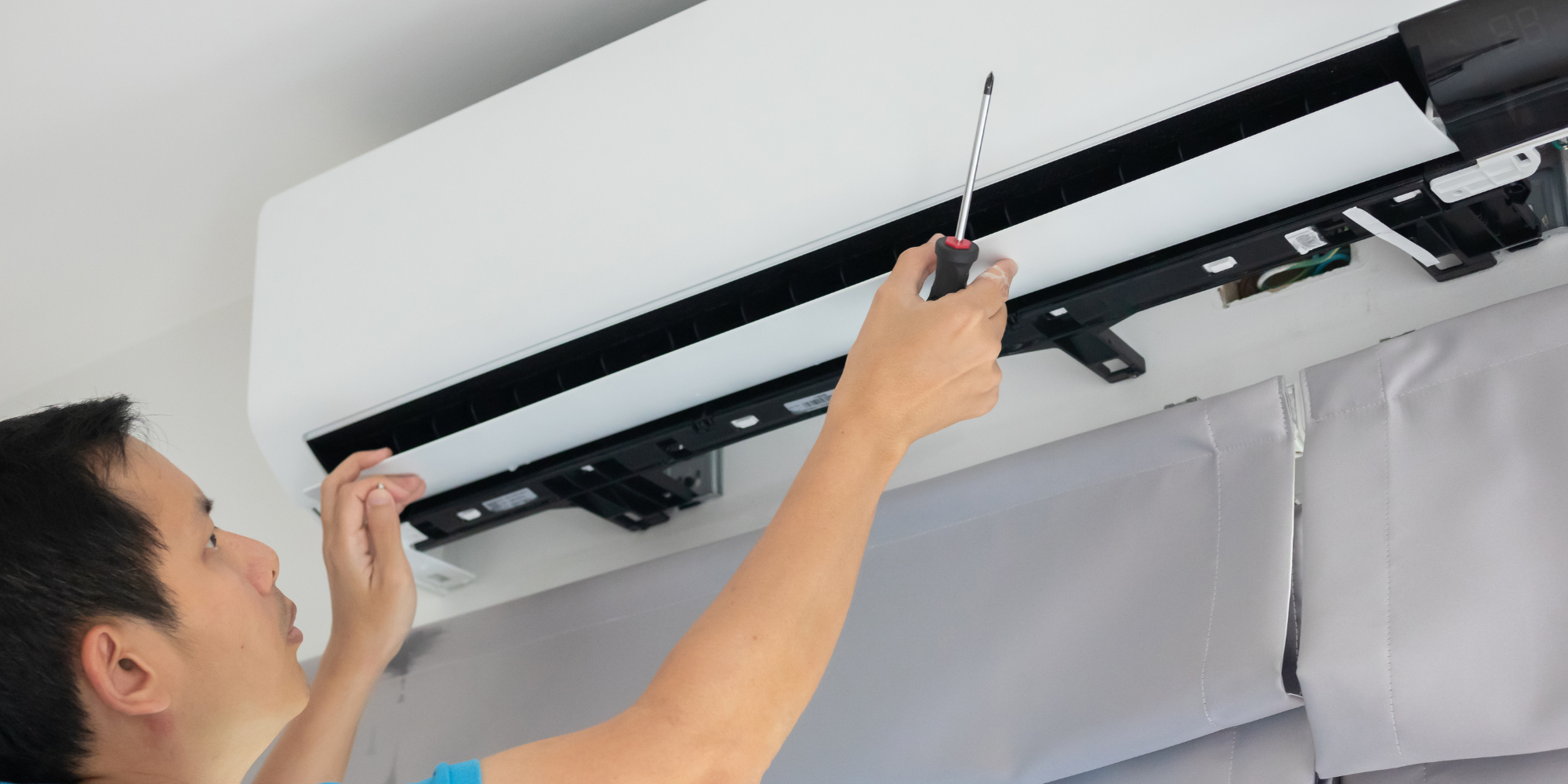A person installing or repairing an air conditioning unit on a ceiling with a screwdriver.