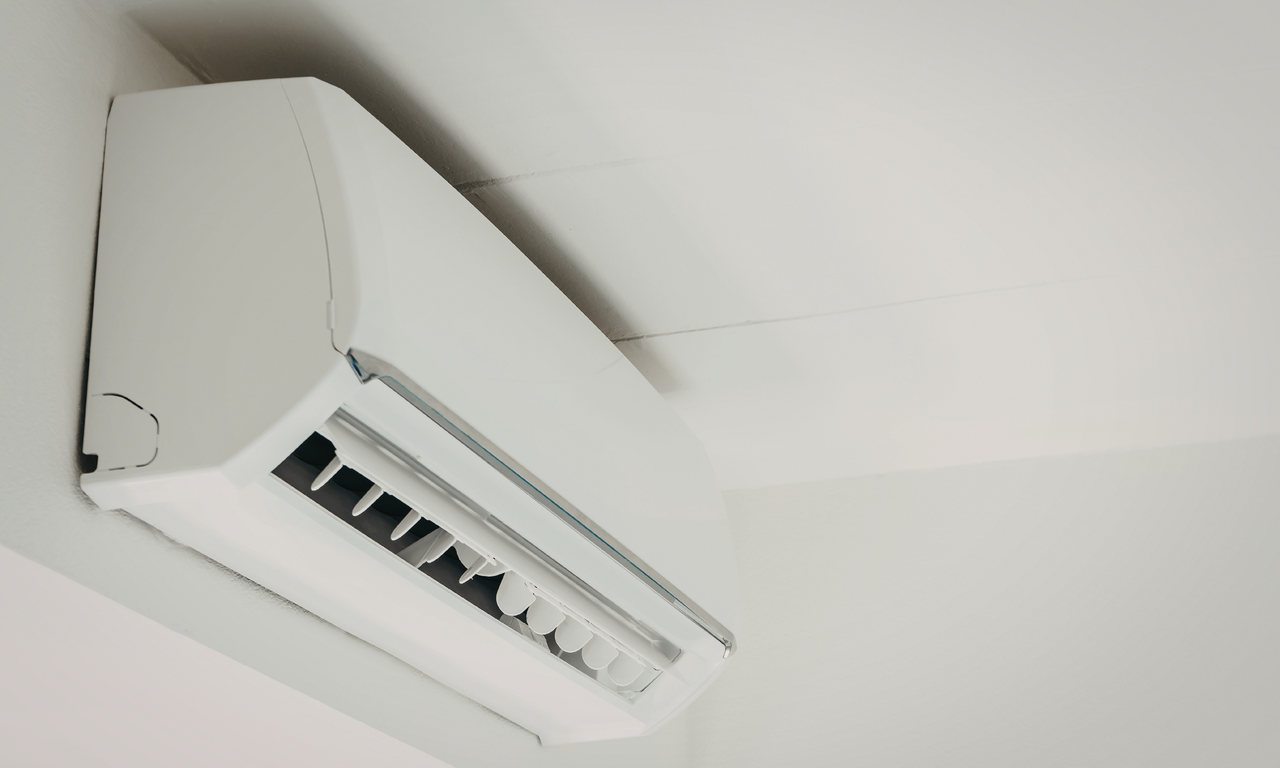 Wall-mounted white air conditioning unit on a white ceiling.