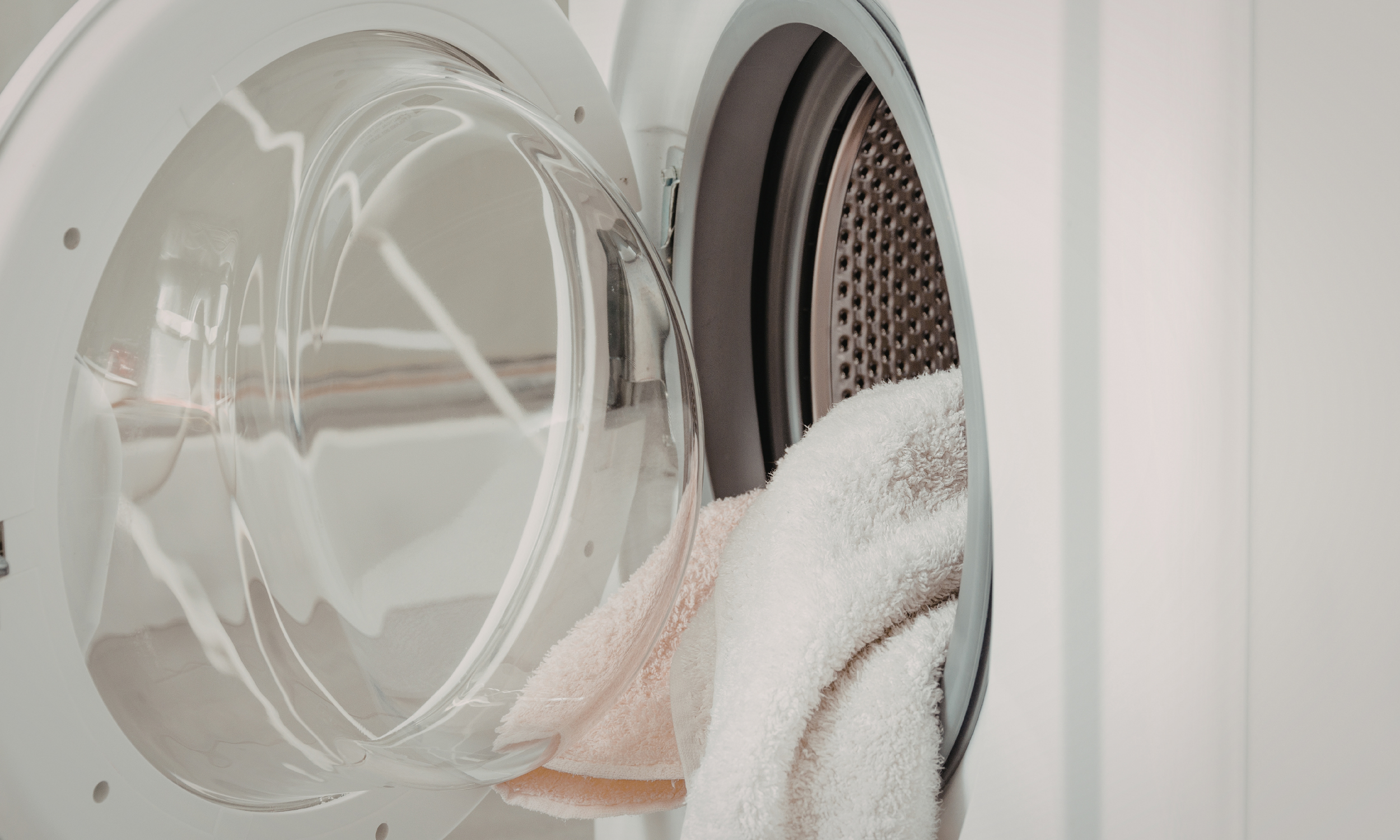 A front-loading washing machine with an open door, with white and light pink towels inside.