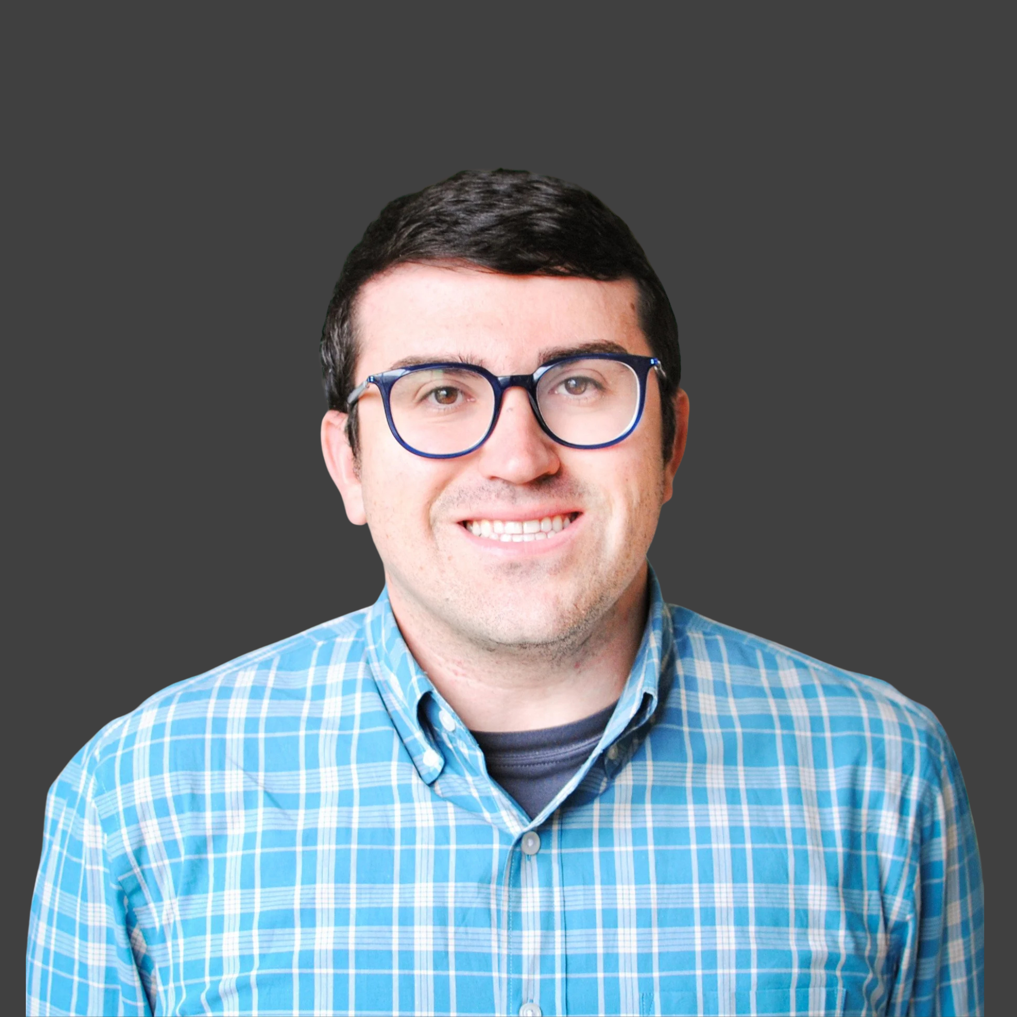 A man with black hair, glasses, and a blue plaid shirt smiling against a dark grey background.