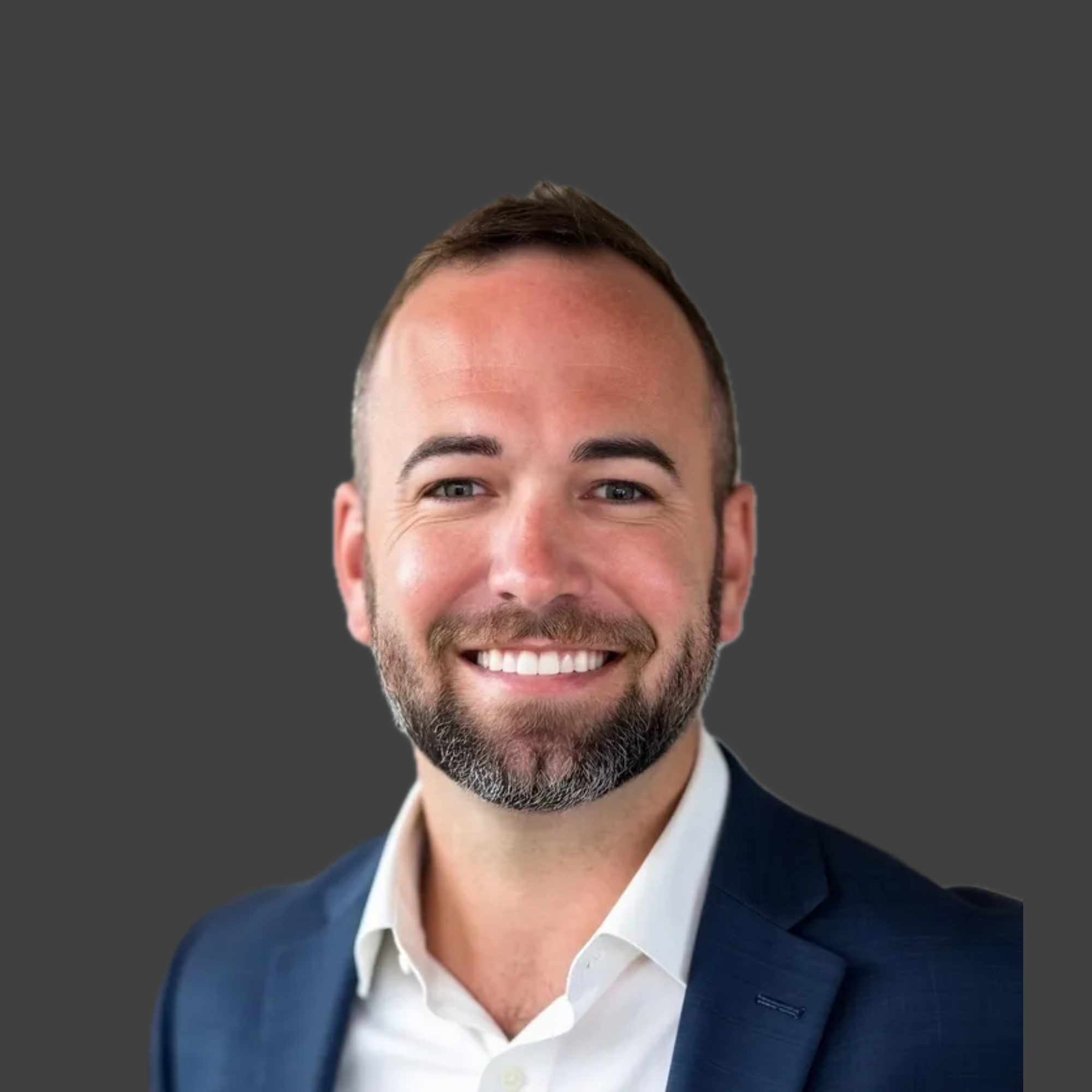 Portrait of a man with short hair, a beard, wearing a navy suit and white shirt, smiling against a dark gray background.