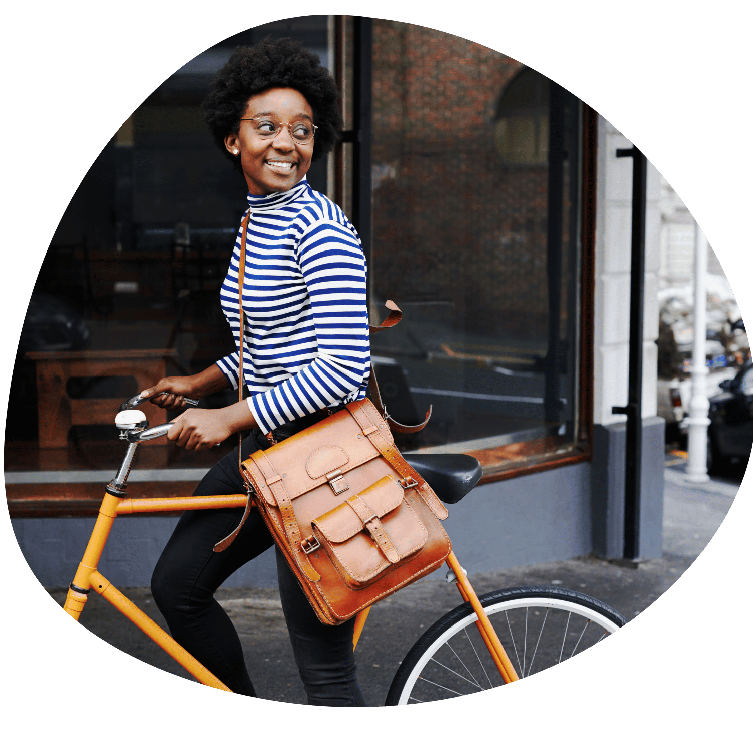 En kvinna med lockigt afro-hår, glasögon och en blåvit randig tröja, som sitter på en orange cykel med en läderväska.