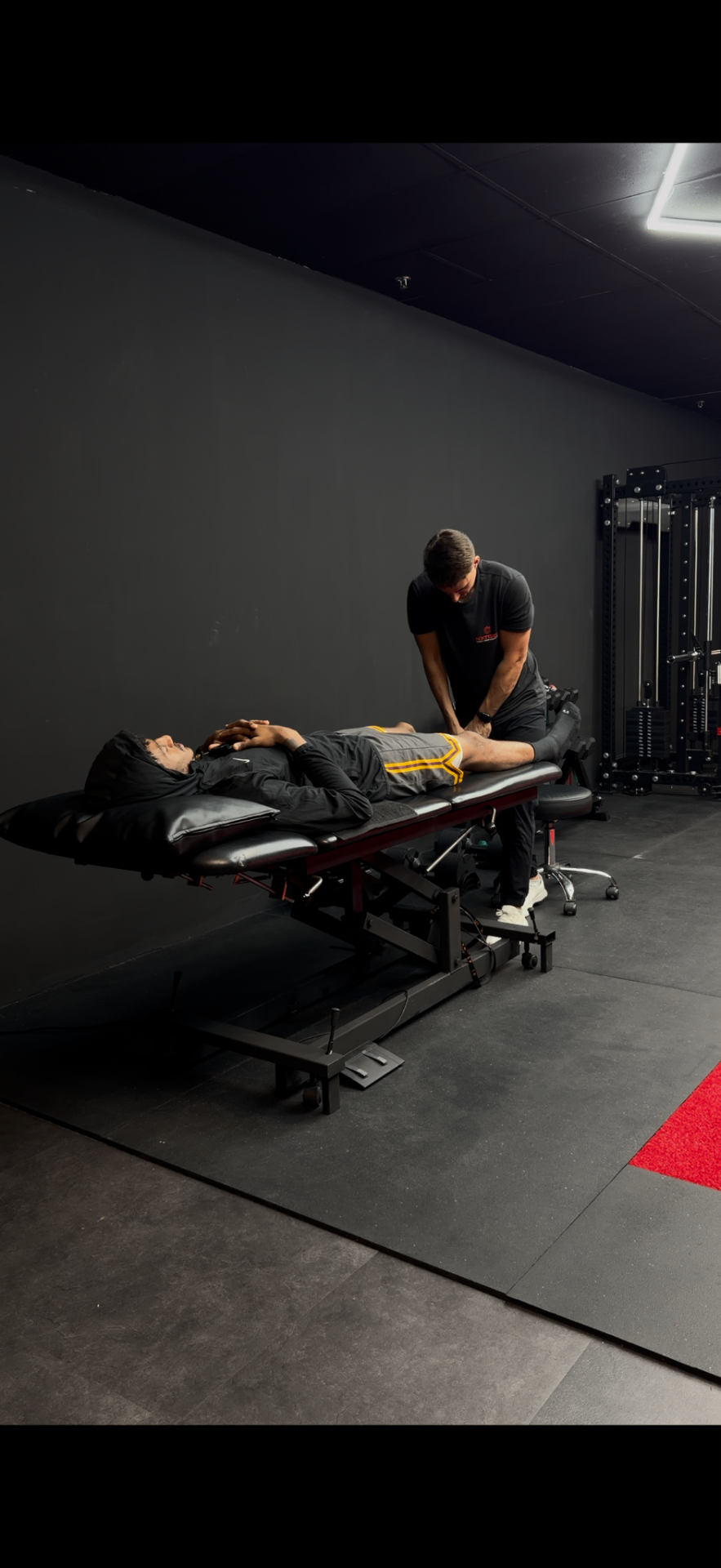 A person lying on a massage table in a dark room receiving a physical therapy session from a therapist.