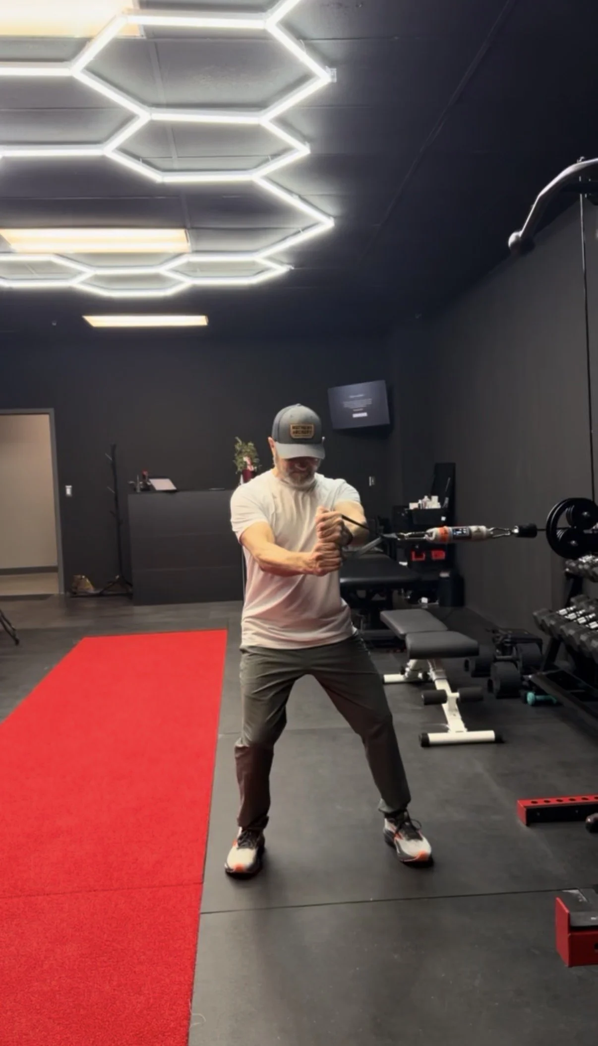 A man is working out with resistance bands in a gym with black walls and modern geometric ceiling lights.
