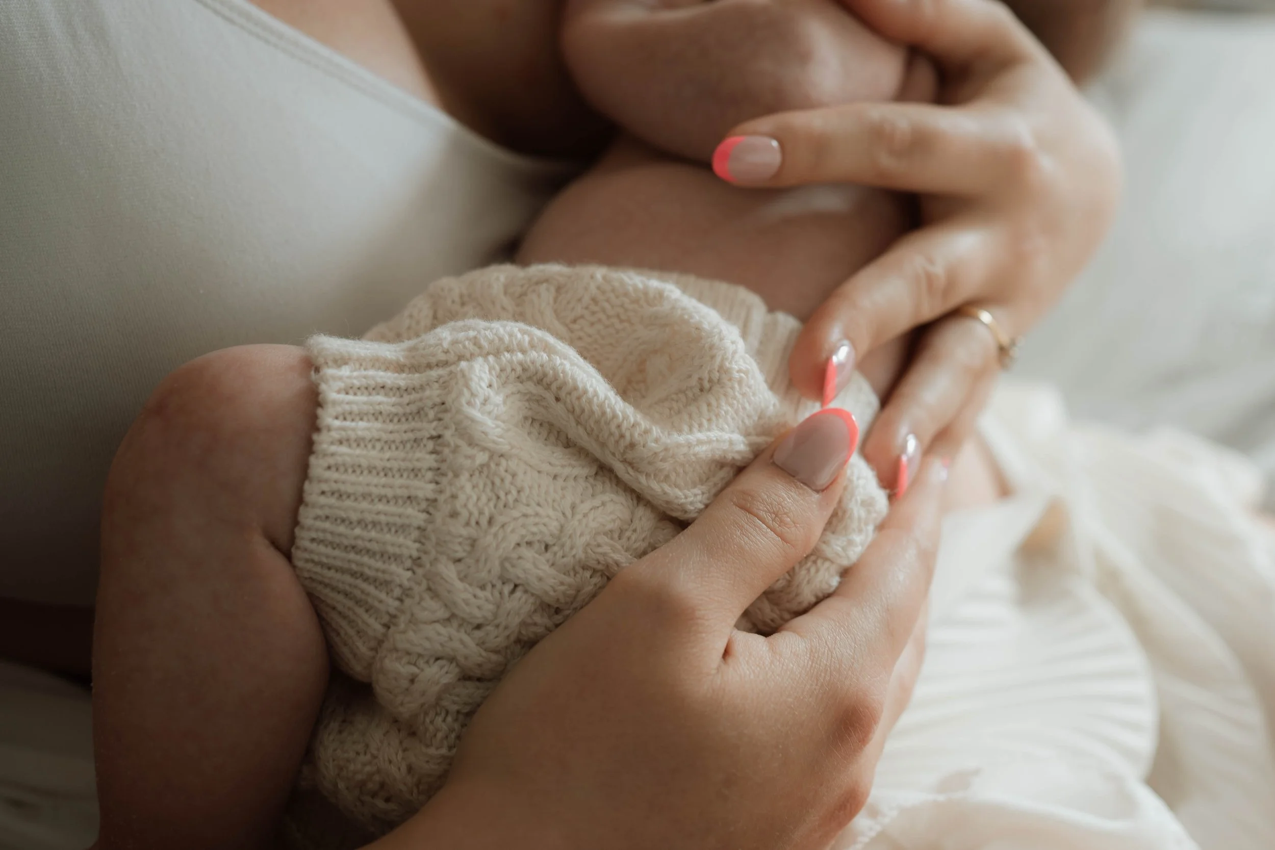 A person holding a baby's hand with a cream-colored knitted blanket covering the baby's arm.