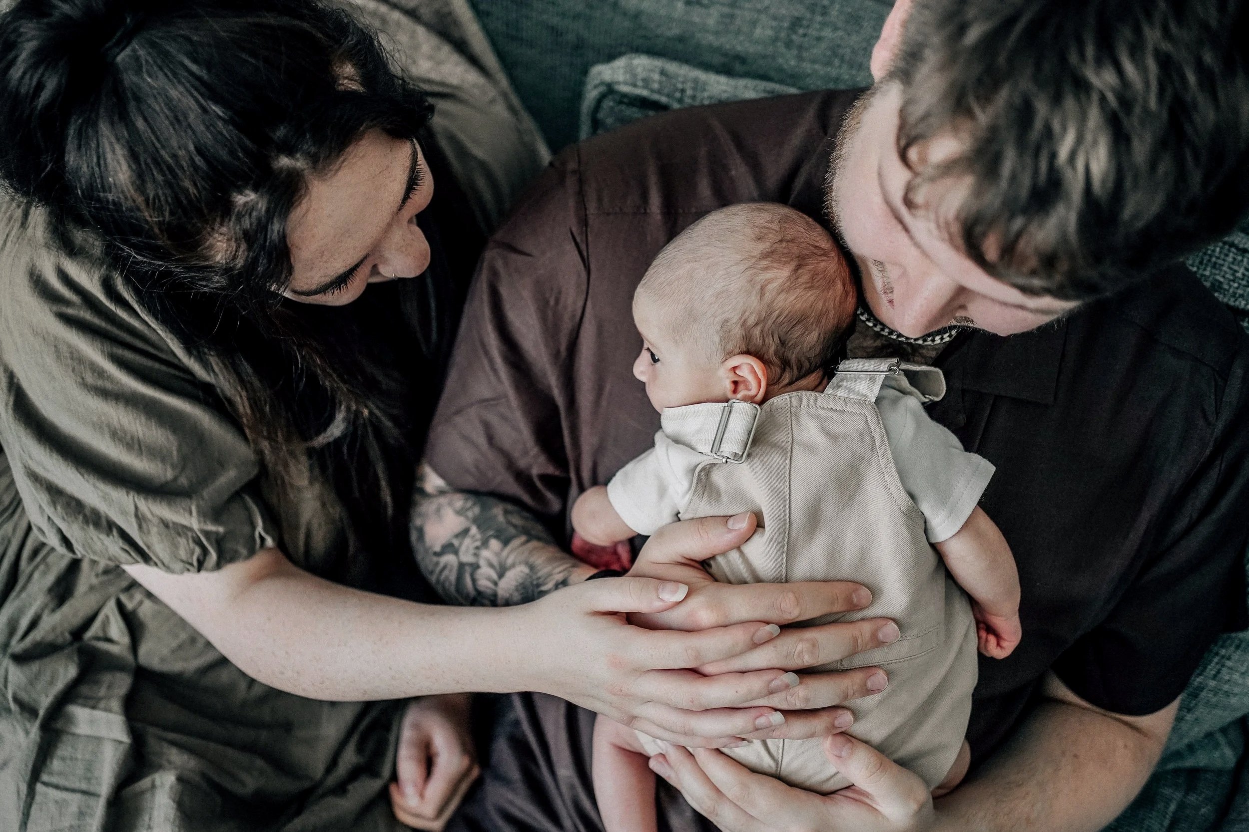 A woman and a man hold a baby, looking at each other affectionately.
