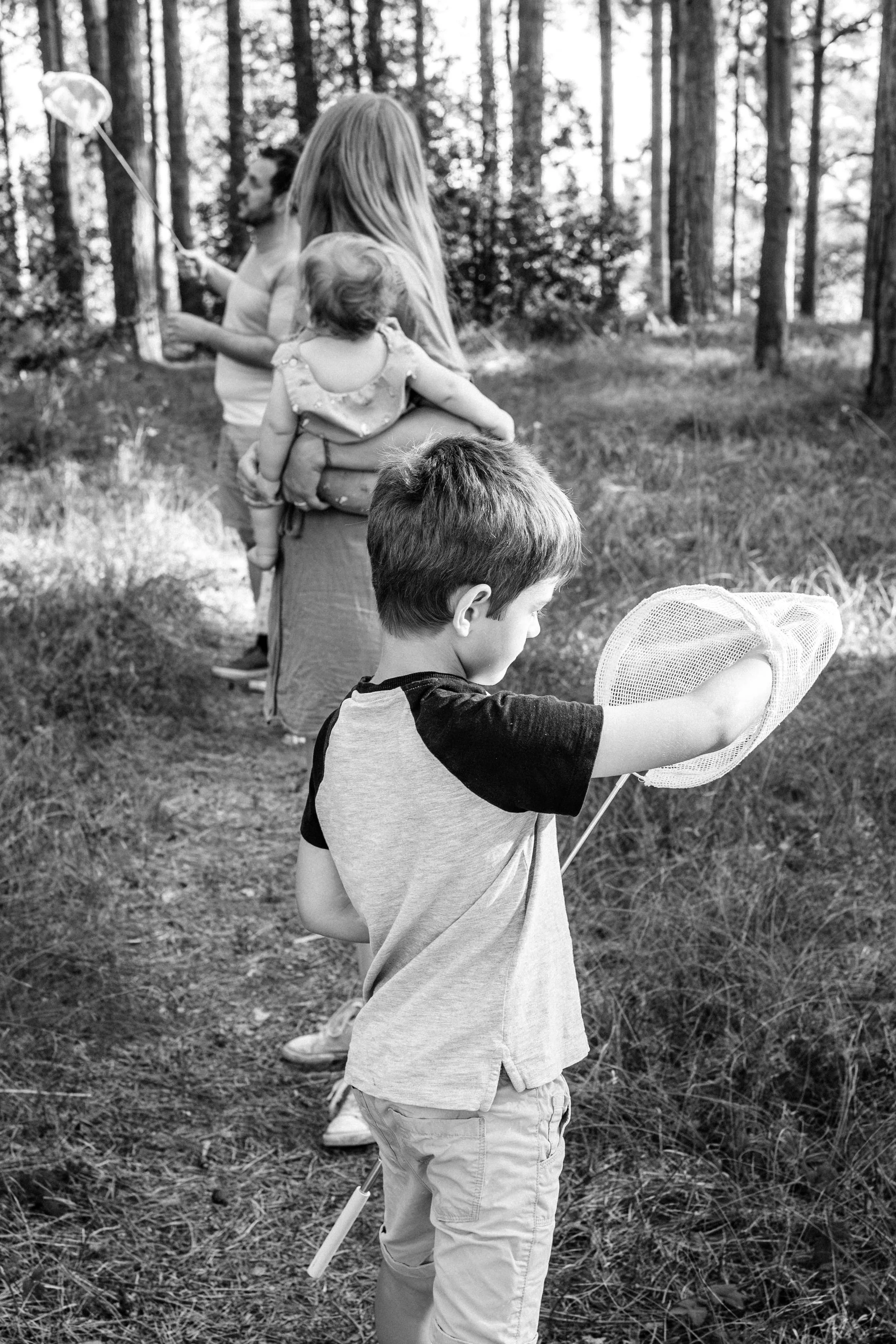 A group of children and adults standing in a line on a forest trail, some holding nets and one holding a balloon.