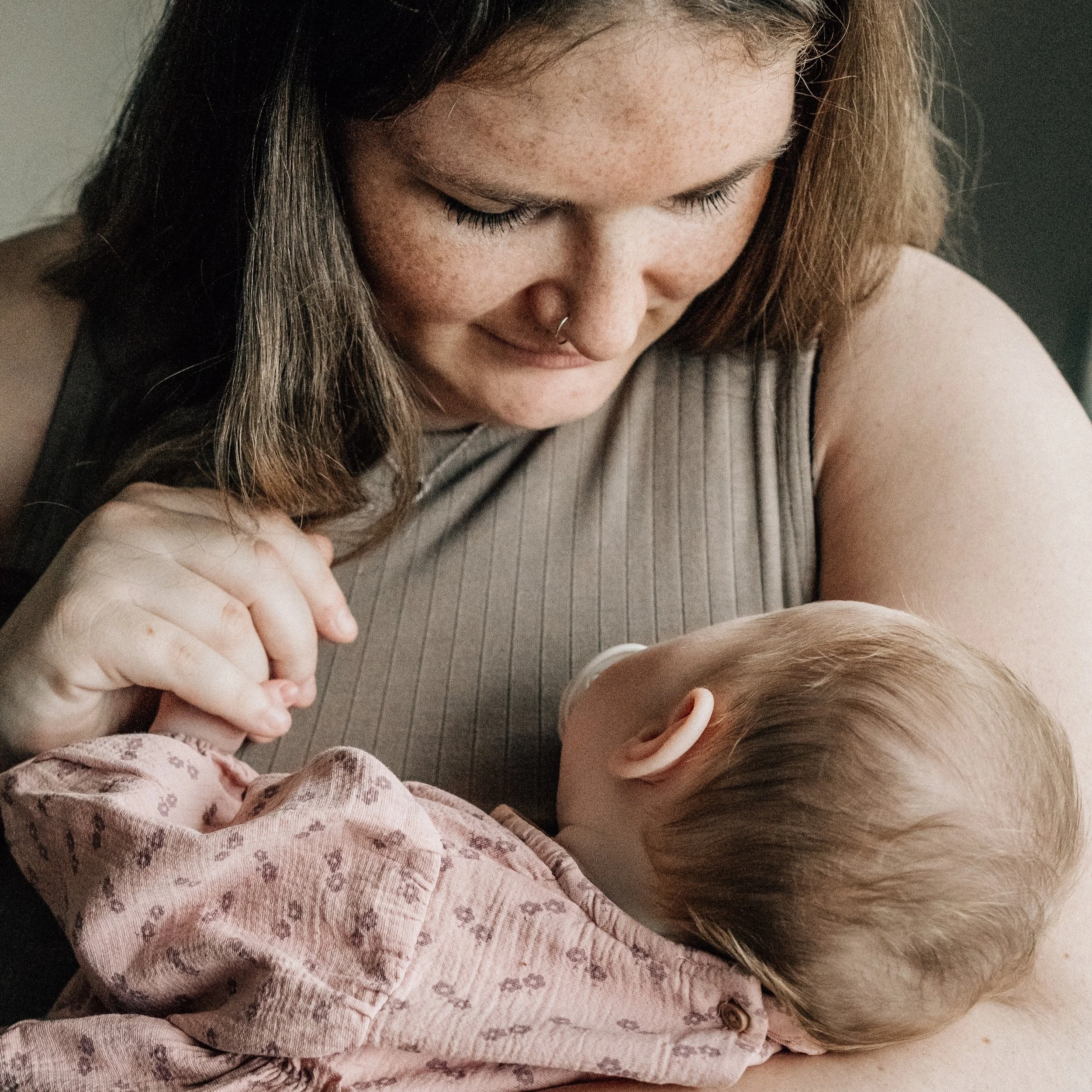 A young woman with light skin and freckles holding and cuddling a small child with light skin and light brown hair, in a tender moment.