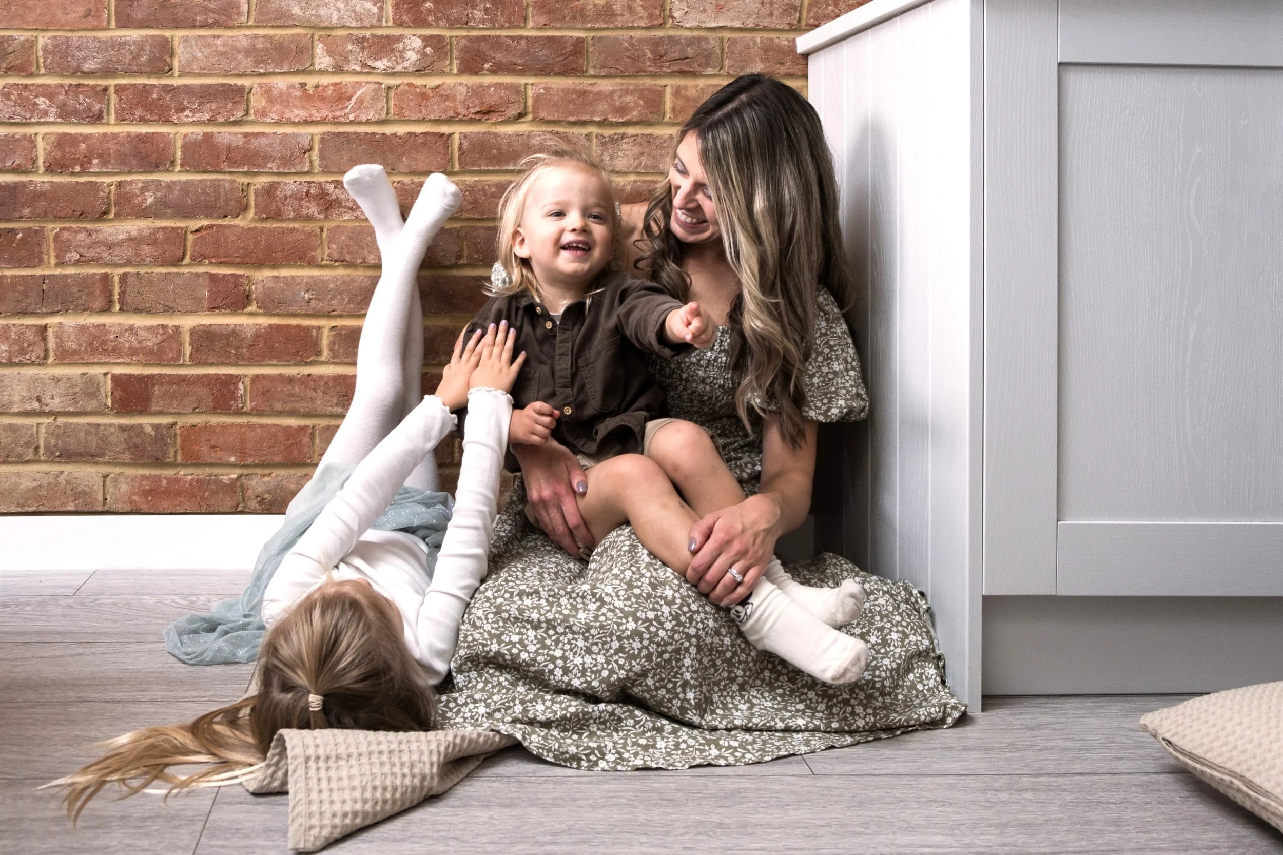 A young girl with blonde hair playing on the floor with toys, while a man stands in the background in a cozy home setting.