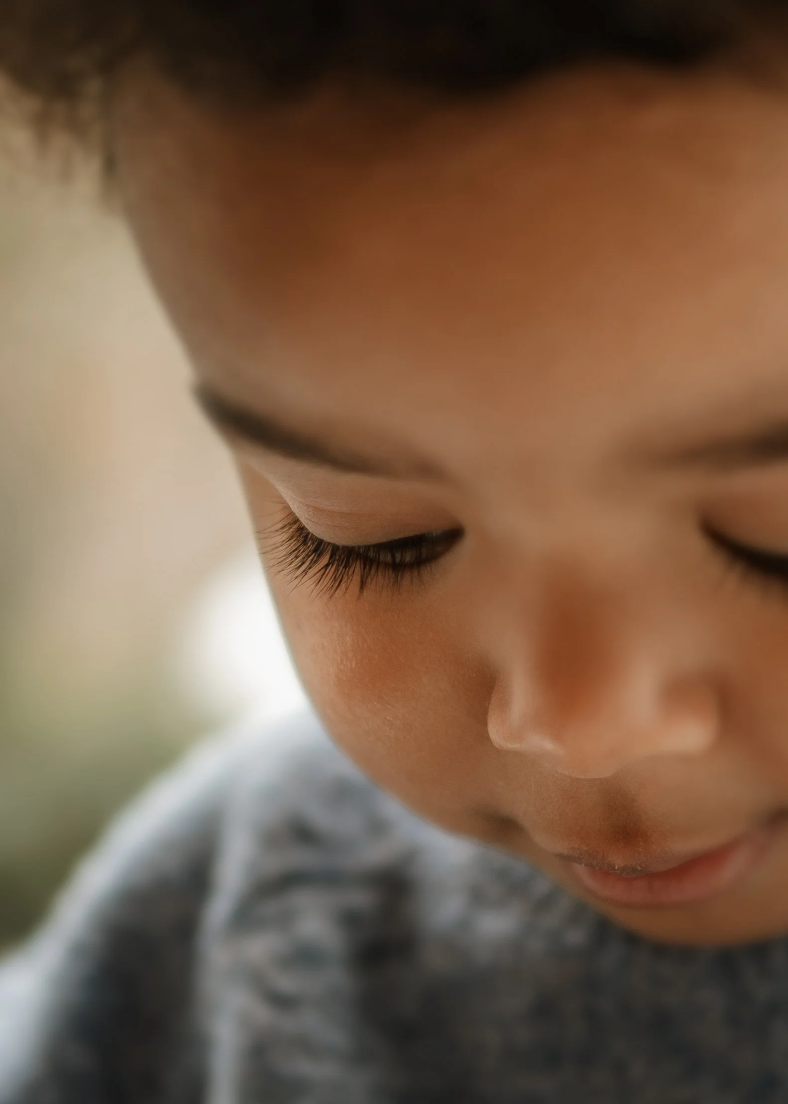 Close-up of a young child's face with closed eyes, showing long eyelashes, soft skin, and part of a gray shirt.