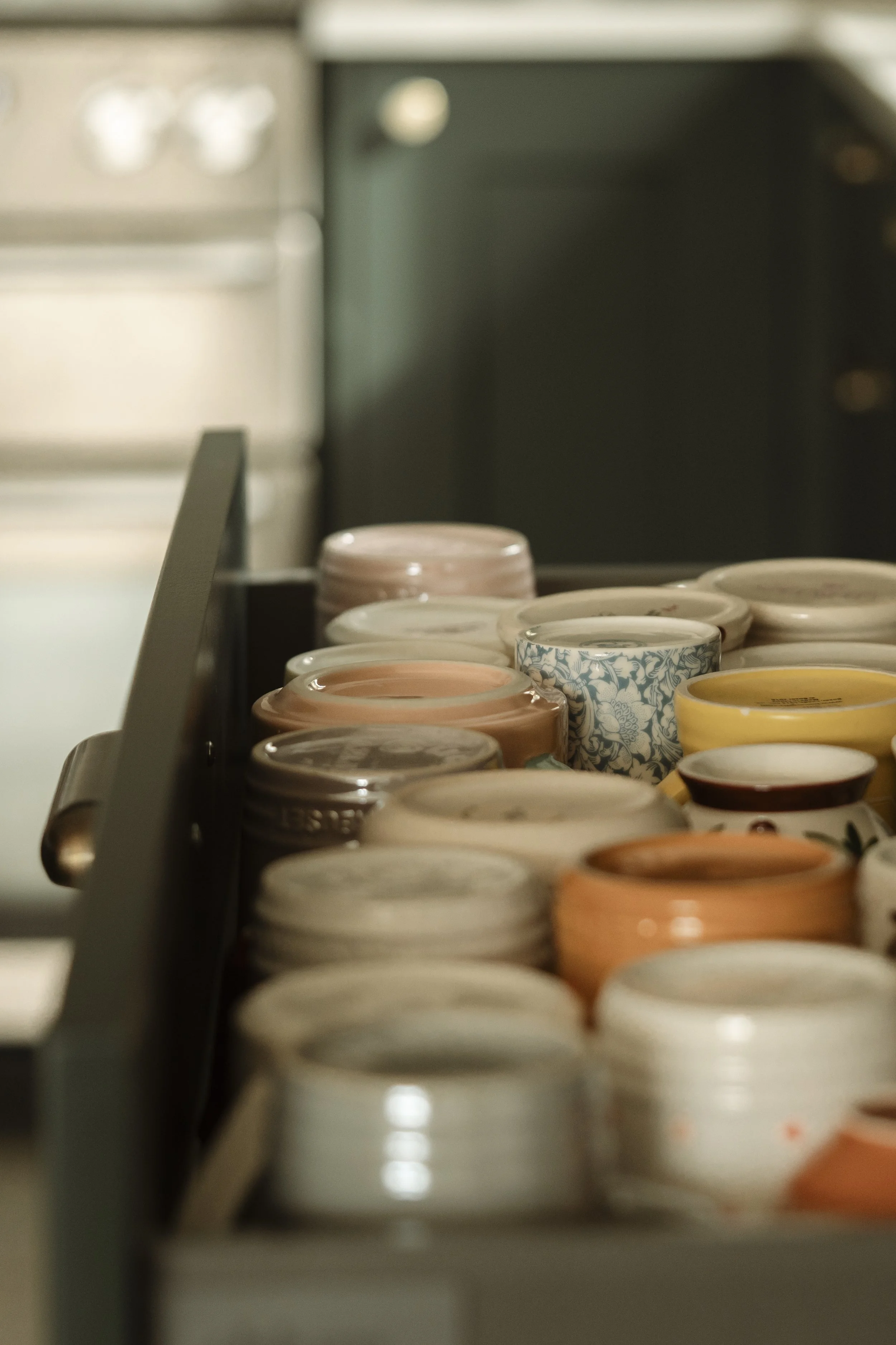 A row of colorful ceramic coffee mugs placed on a kitchen countertop, with some stacked and others arranged side by side.