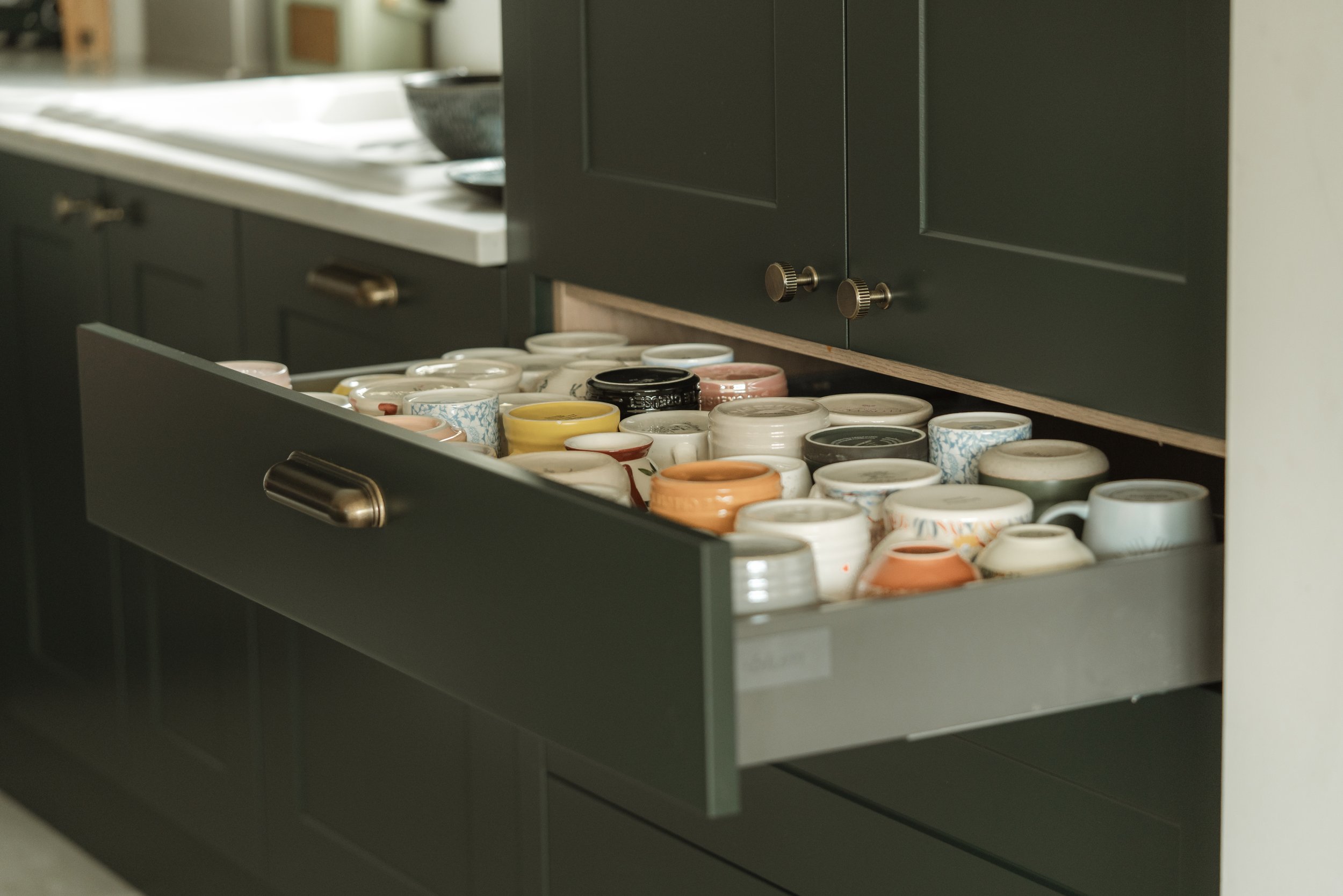 Open kitchen drawer filled with various coffee mugs and teacups in a modern kitchen.