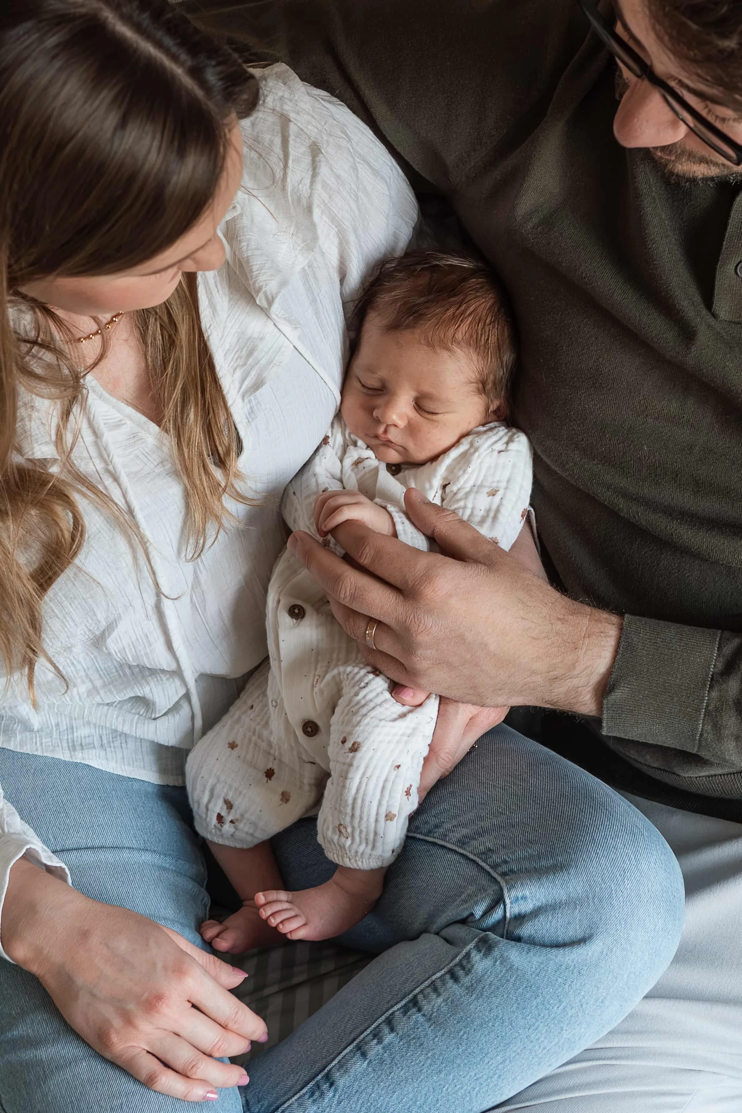 A newborn baby sleeping peacefully while being held by three adults, two women and one man, all sitting close together.
