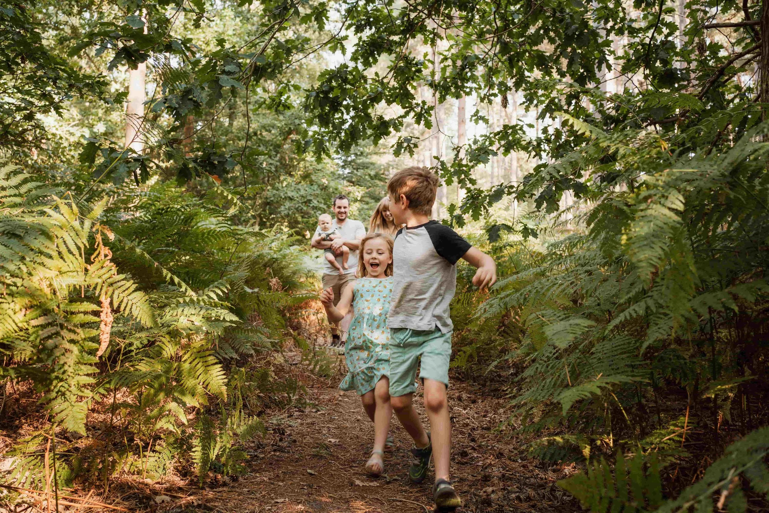 Children running and playing in a wooded forest area with lush green foliage.