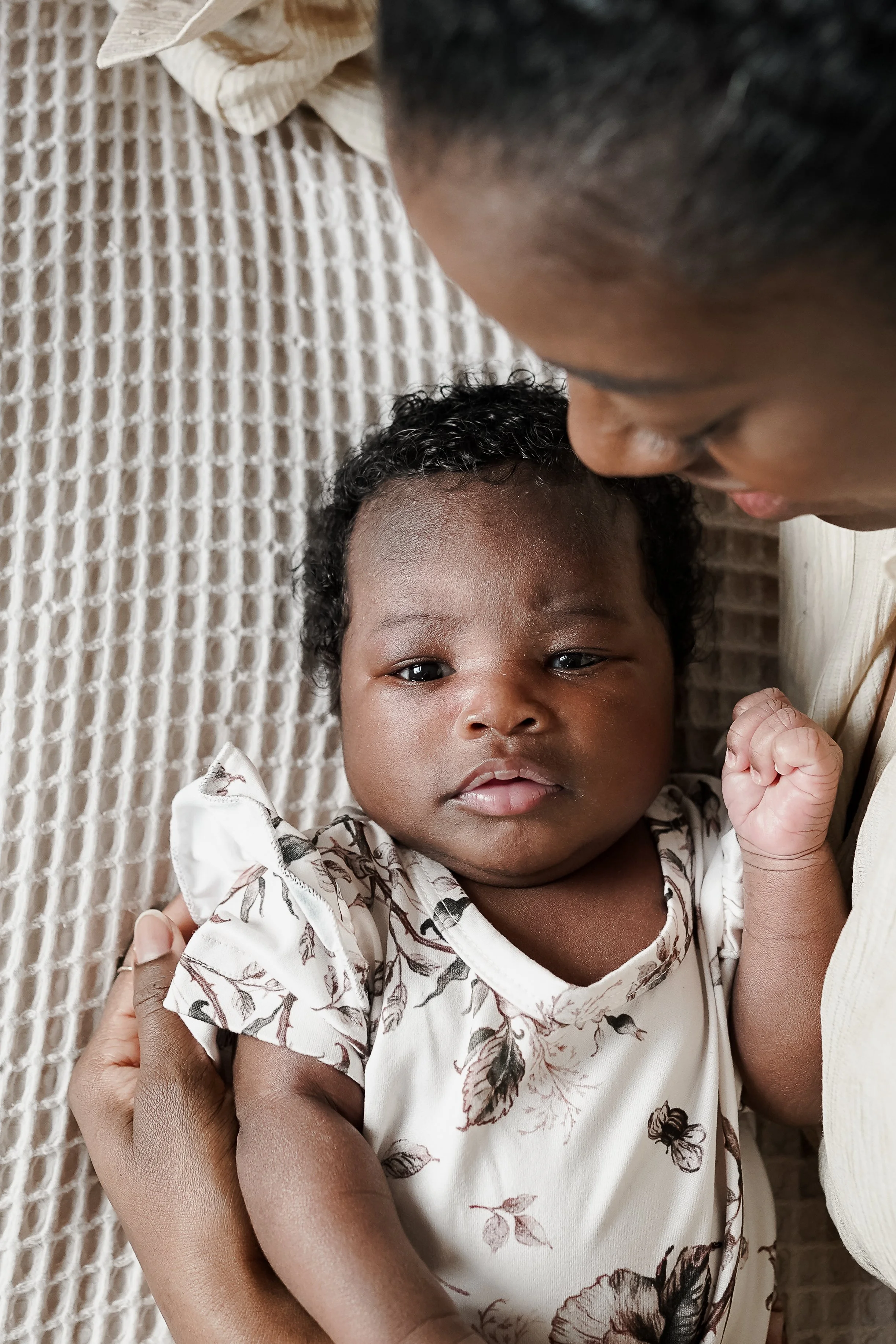 Close-up of a young child lying on a blanket, being held and comforted by an adult, with the adult's face close to the child's.