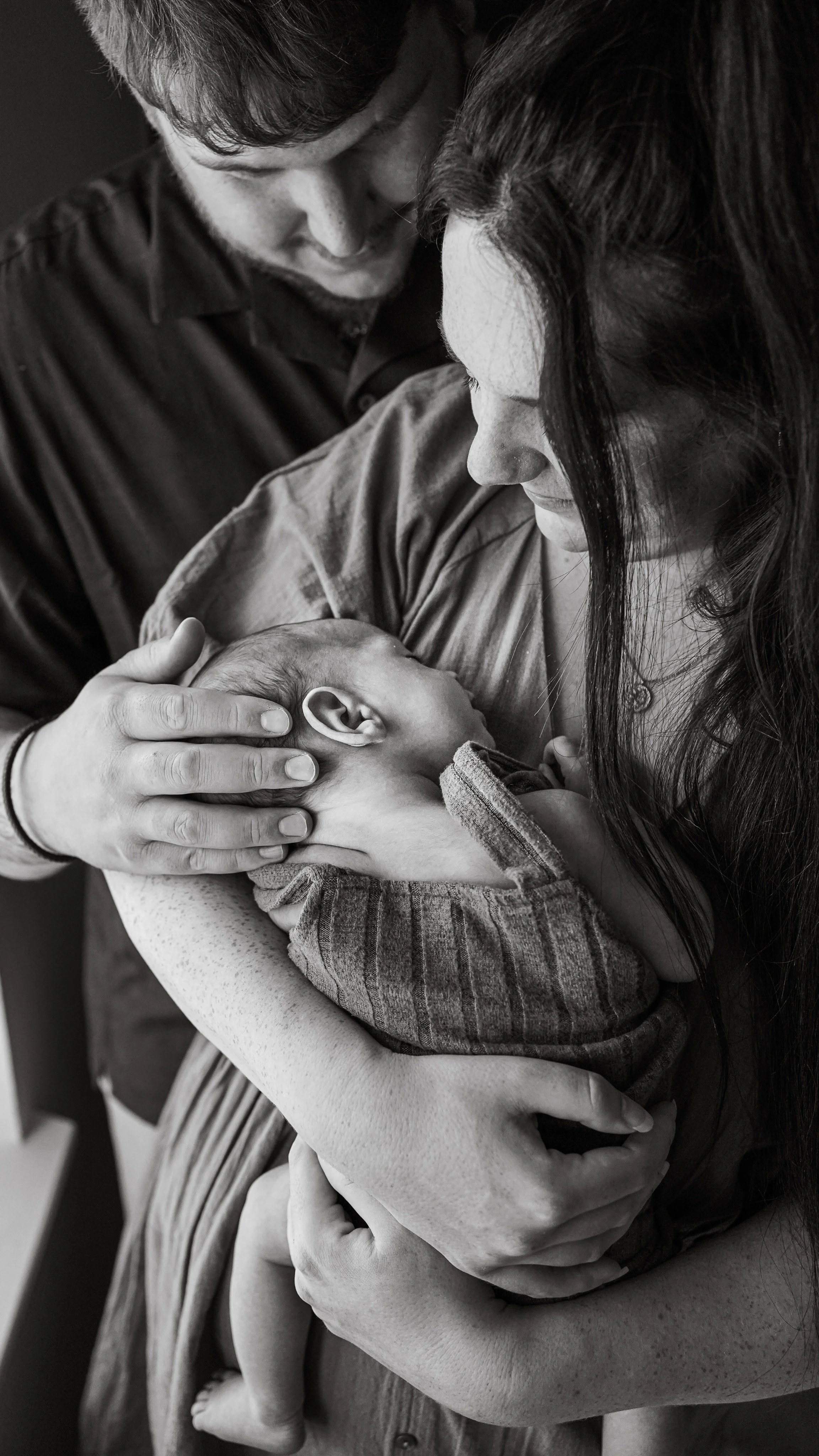 A woman holding a baby close to her chest with two people lovingly touching the baby's head in a black-and-white photo.