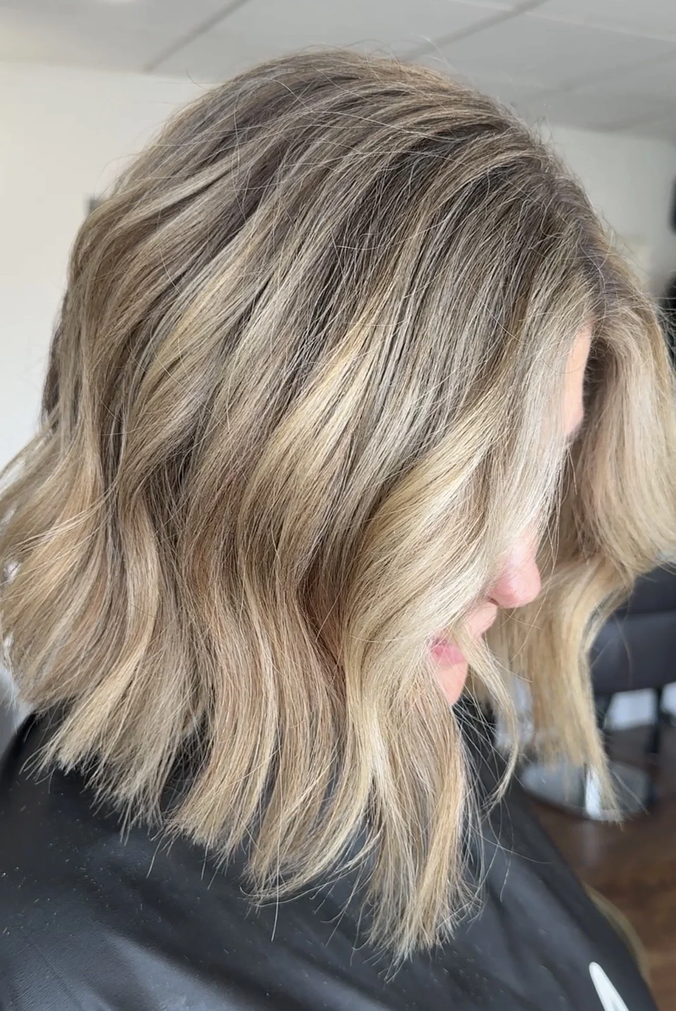 A woman with shoulder-length blond hair styled in loose waves, sitting in a salon chair.
