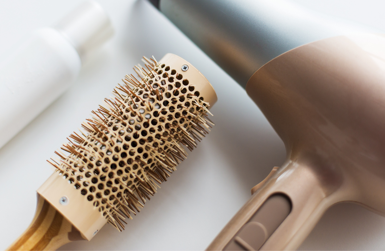 Close-up of a beige hairbrush and a beige hairdryer on a white surface.