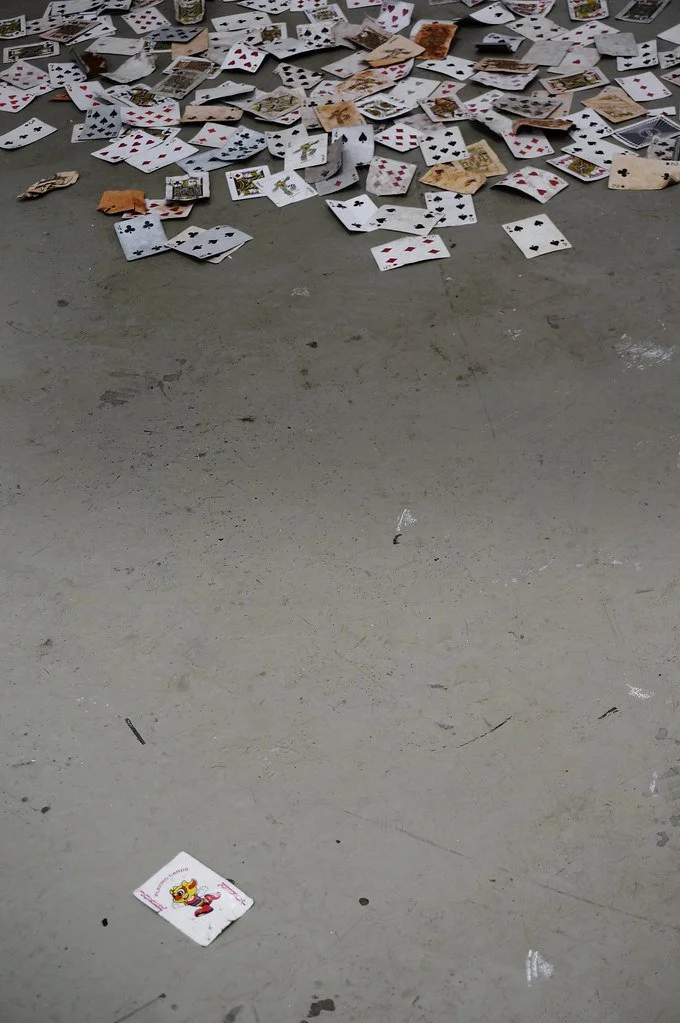Scattered playing cards on a gray concrete floor, with a single card featuring a cartoon character in the foreground.