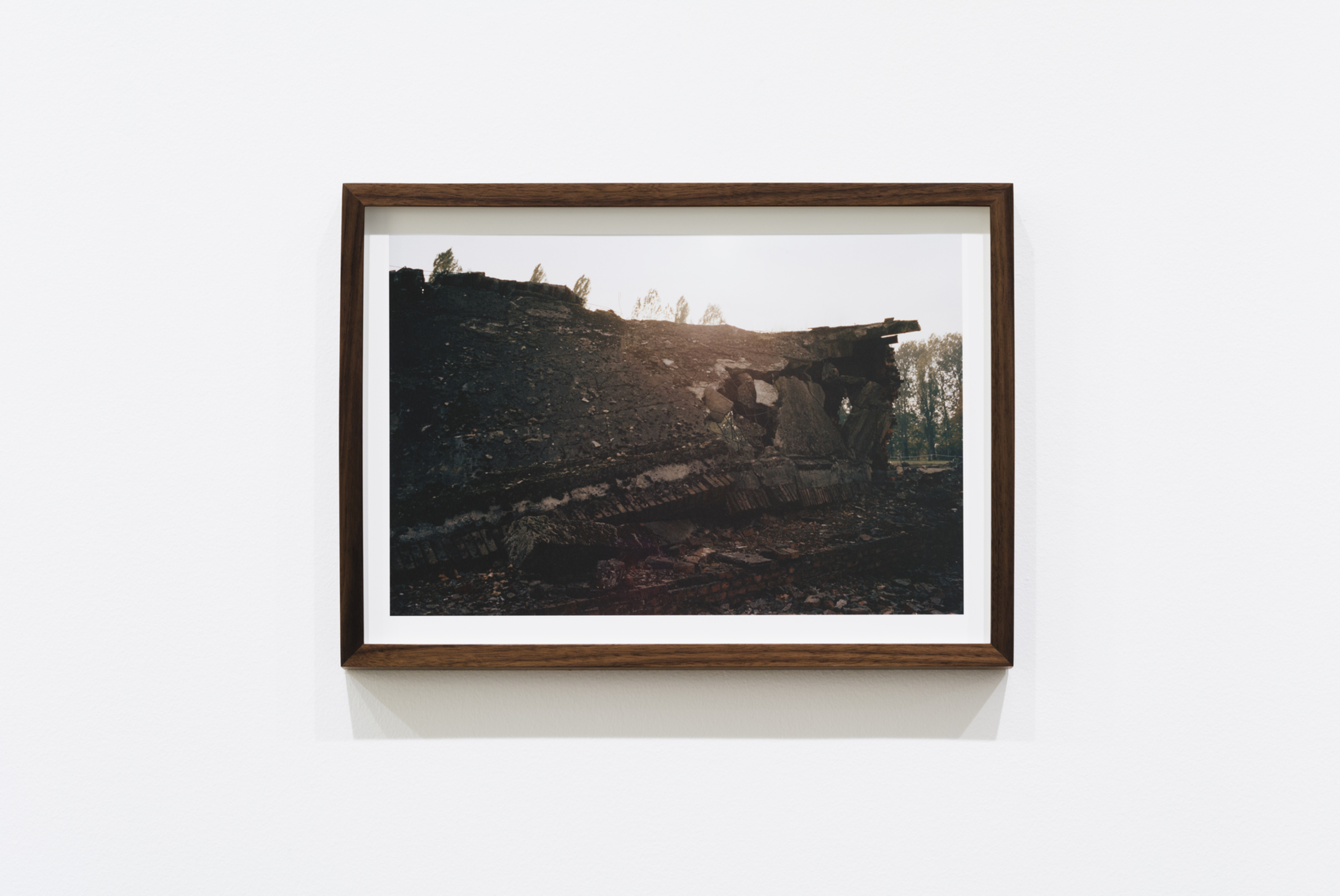 A framed photograph of the aftermath of a fire or explosion, showing damaged and burned terrain with scattered debris and some trees in the background.