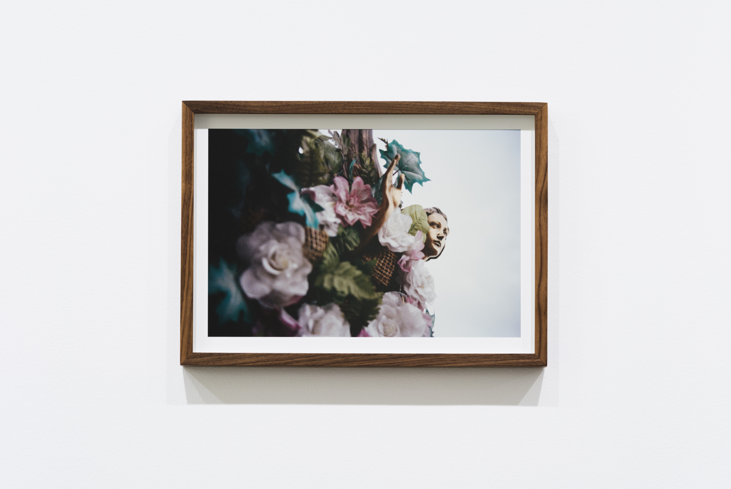 A framed photo on a white wall showing a woman with floral arrangements in front of her face and a large American flag in the background.
