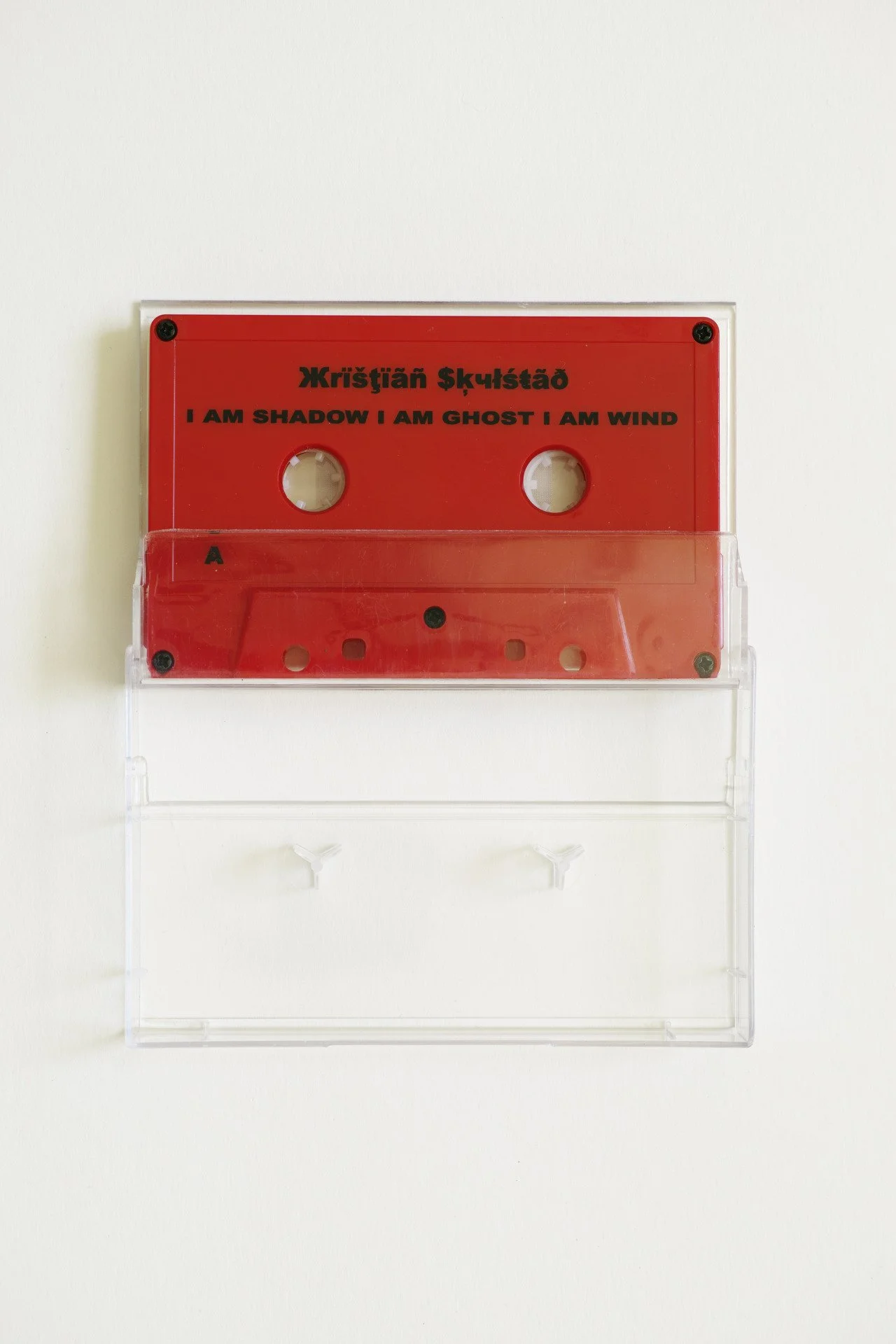 A red cassette tape with black text on a white background. The album I am Shadow I am Ghost I am Wind. Frøya Records.