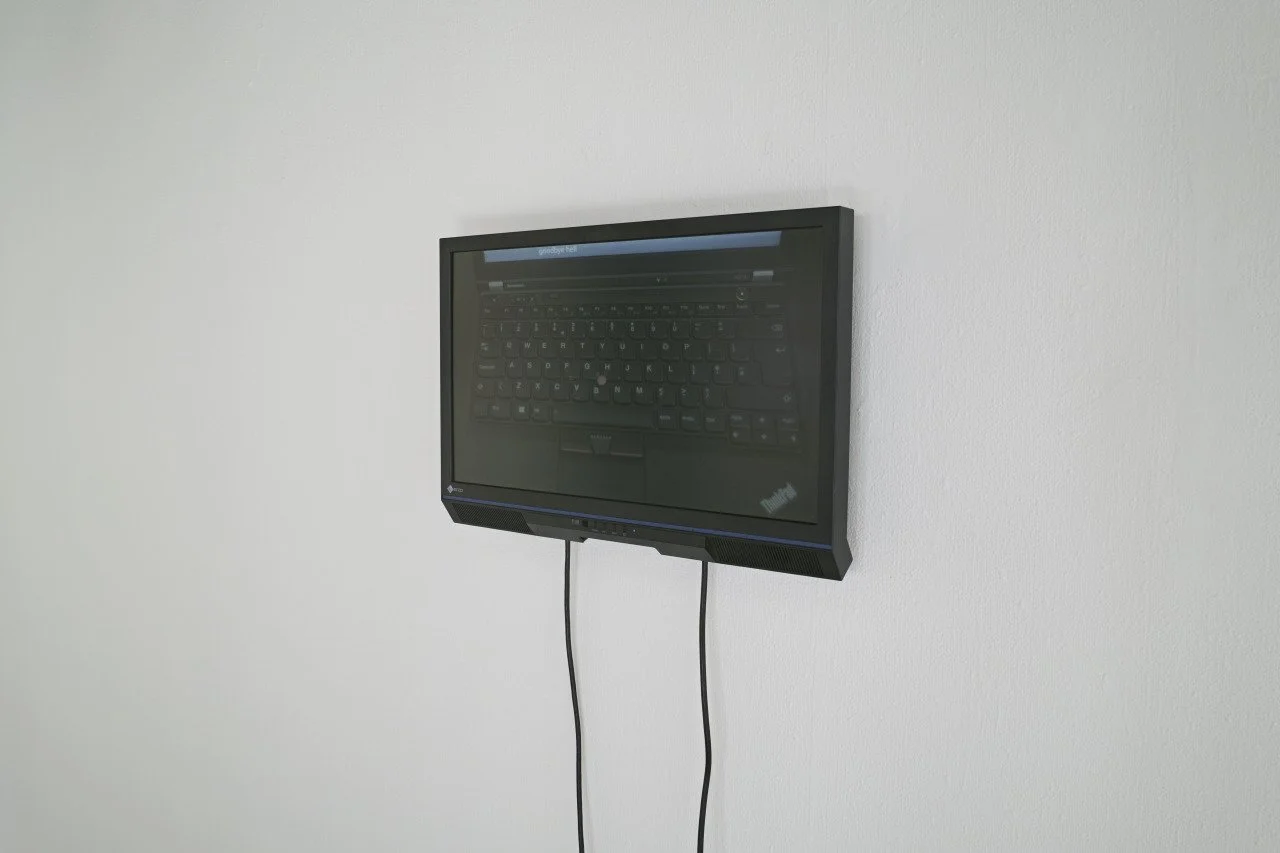 Wall-mounted monitor displaying a keyboard, with two cables hanging down. 