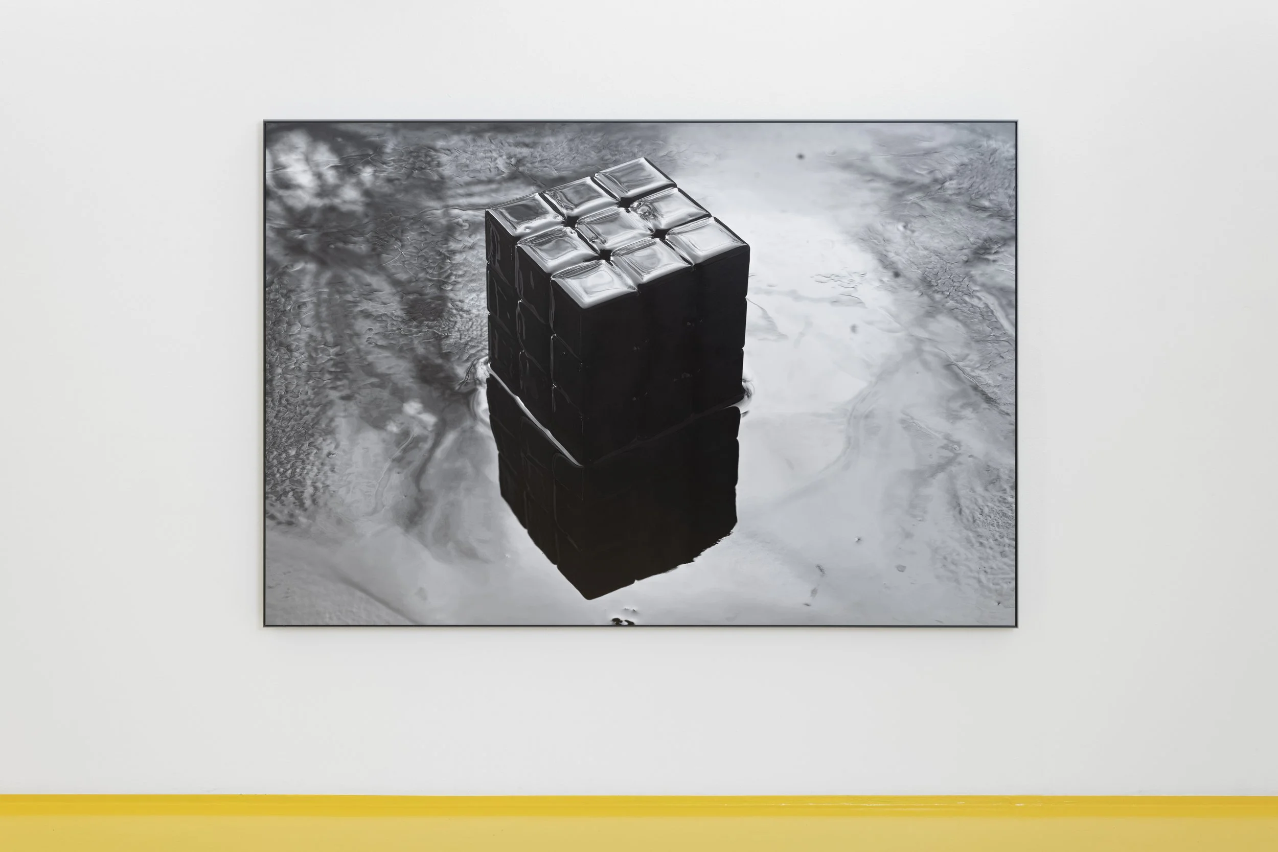 Black Rubik's Cube floating in water, with its reflection visible on the surface. Fotogalleriet in Oslo. Vårutstillingen.
