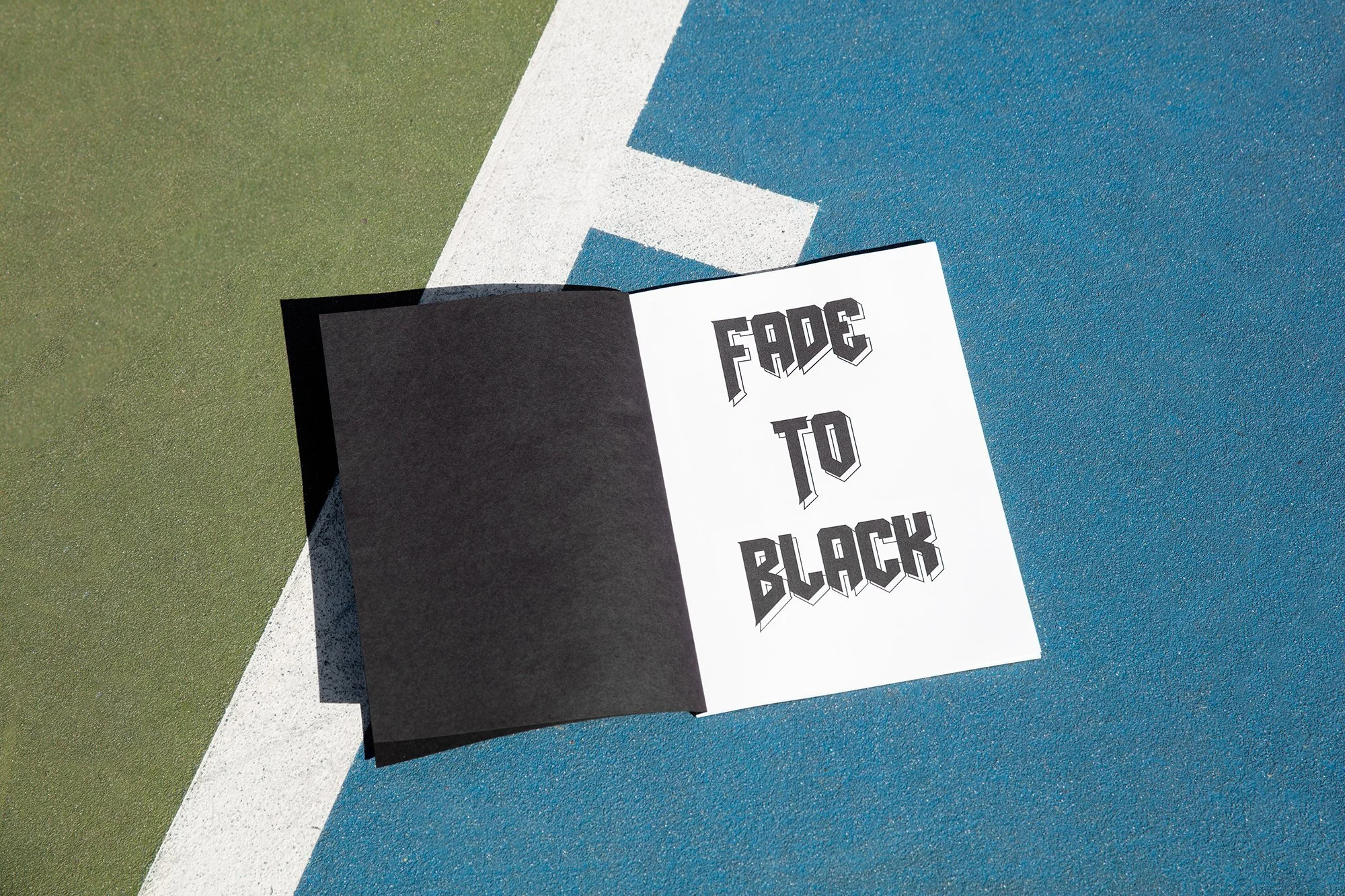 Open booklet on a blue and green sports court with the words "FADE TO BLACK" in bold, stylized letters.