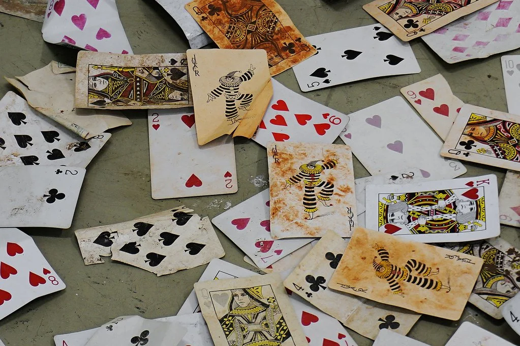 Scattered playing cards, including some with a circus clown design, across a surface, with some cards overlapping and worn.