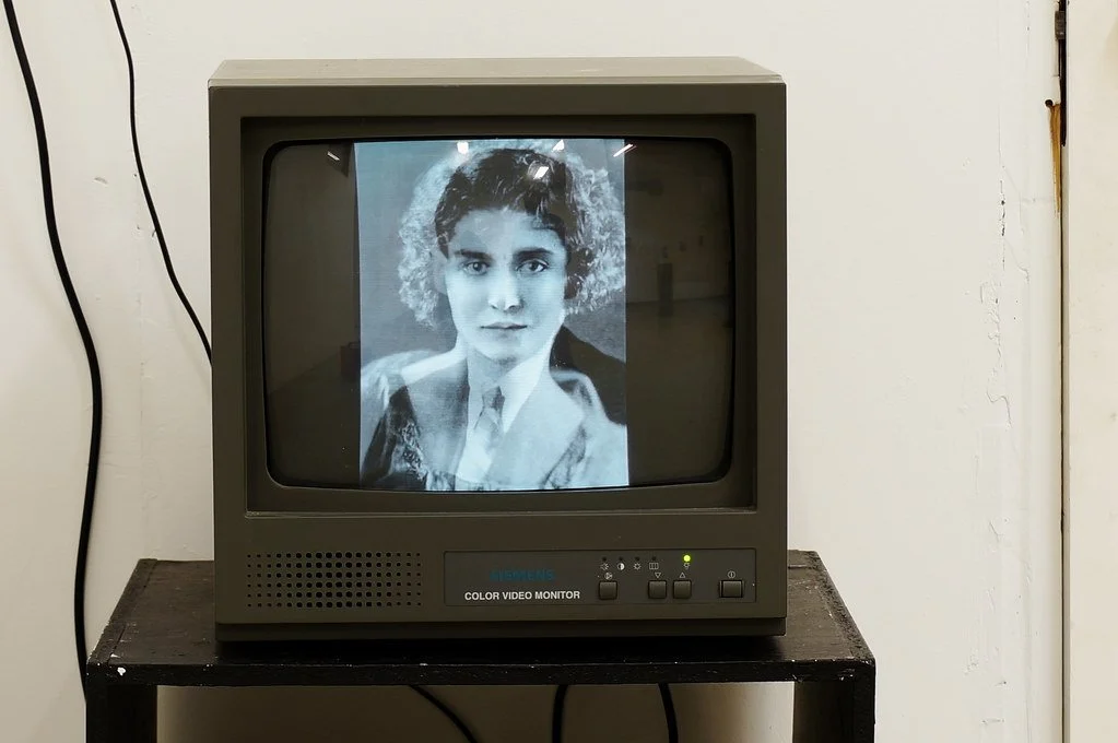 Black and white photograph of a woman with short dark hair, displayed on a vintage CRT monitor.