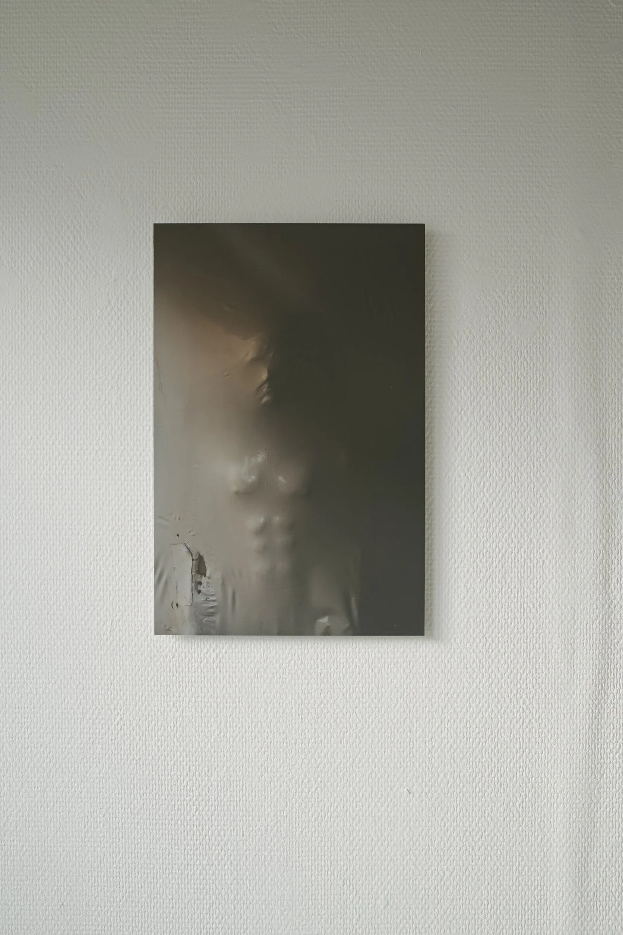 A metal sculpture of a man's face coming out of plastic material.