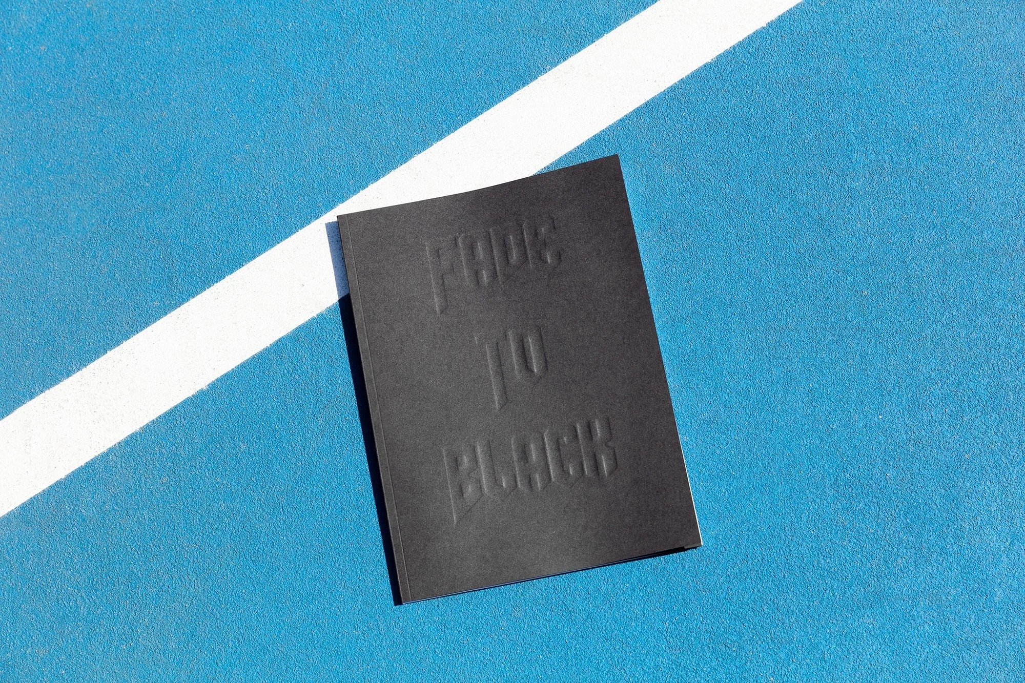 Black booklet with embossed text reading 'HPC 10 BLOCK' lying on a blue sports court with a white line.