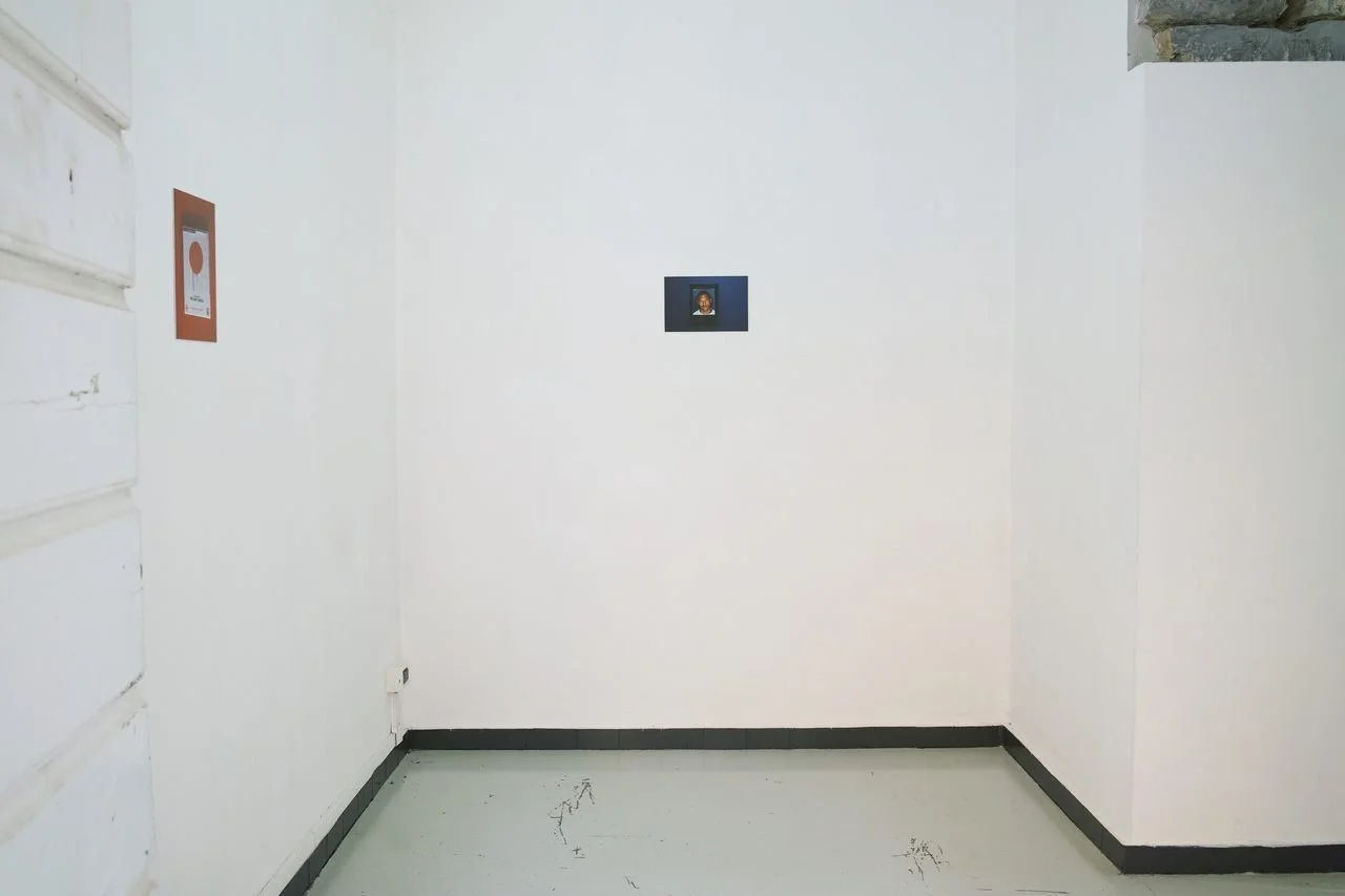 Empty gallery corner, space 4235 Genova, with two small framed artworks on white walls and a white floor.