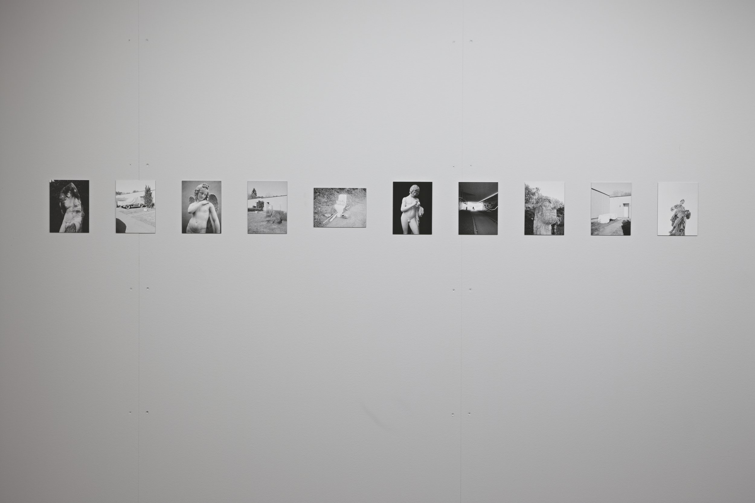 A series of small black and white photographs mounted on a white gallery wall, arranged in a horizontal line.